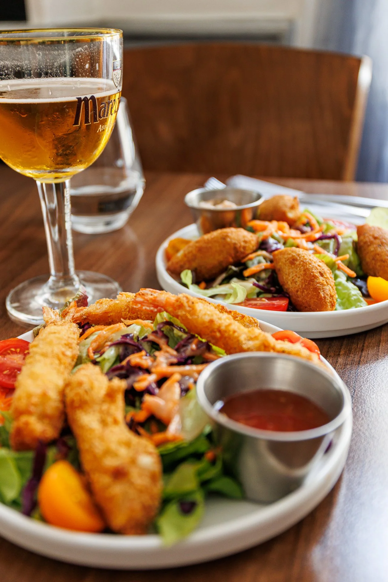 Assiette de salade avec des morceaux de poulet frits, des légumes, et une sauce, accompagnée d'un verre de bière blonde et d'un verre d'eau.