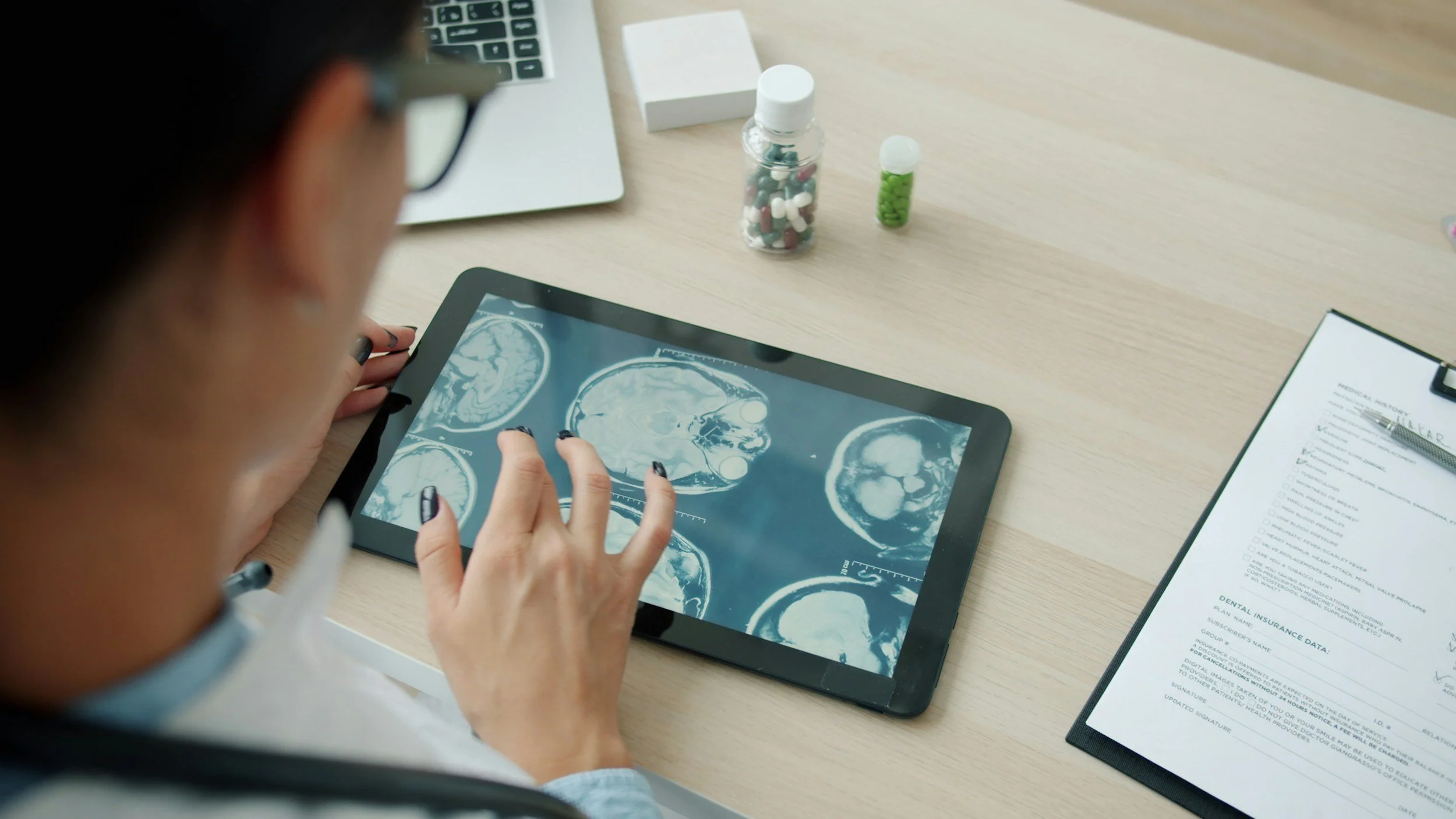 A person in glasses looks at a tablet displaying brain scan images.