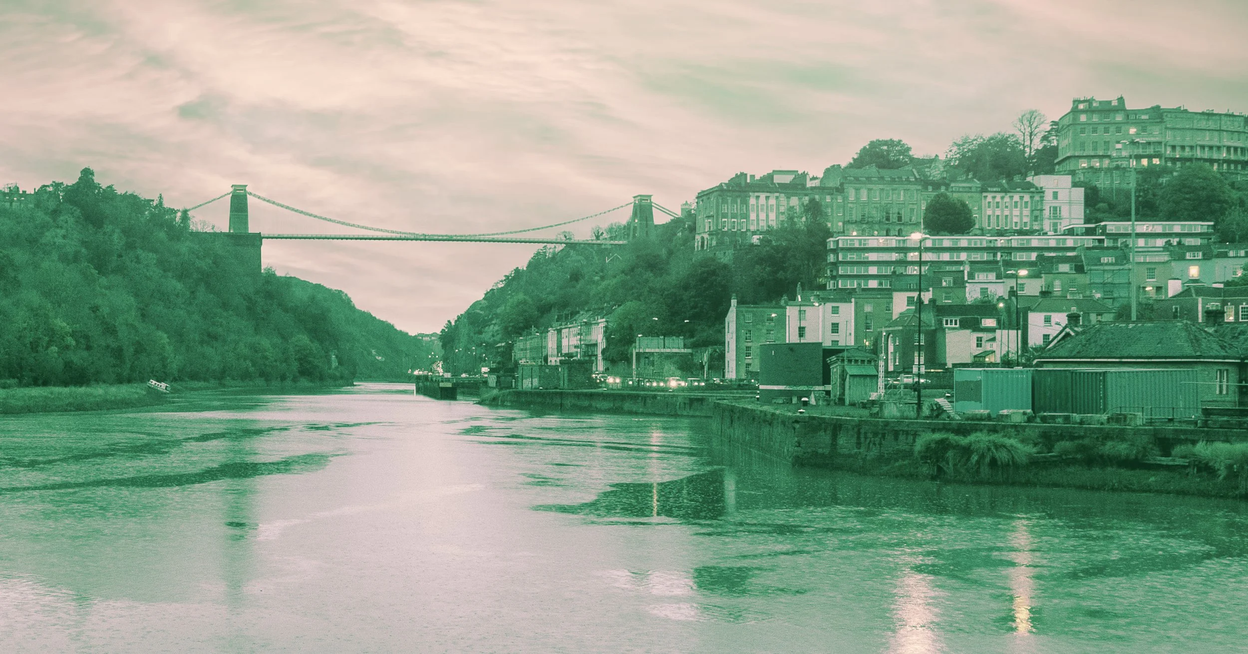 A river flowing through a city with buildings on hillside, and a bridge spanning across the river in the background.