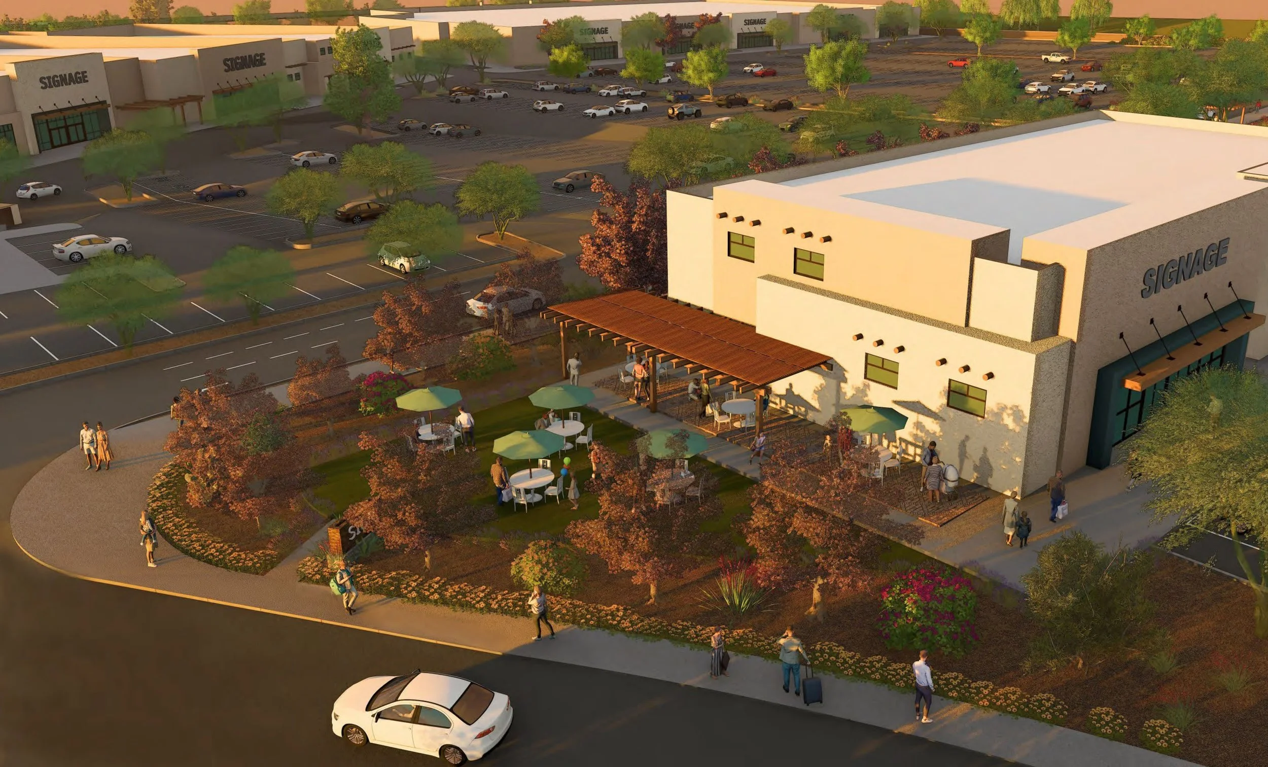 An outdoor area of a shopping complex with a sitting area featuring tables with umbrellas, trees, and flowers, and a parking lot filled with cars in the background.