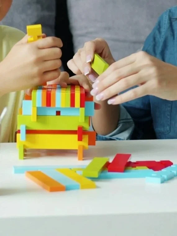 Two people playing with colorful building blocks, assembling a structure on a white table.