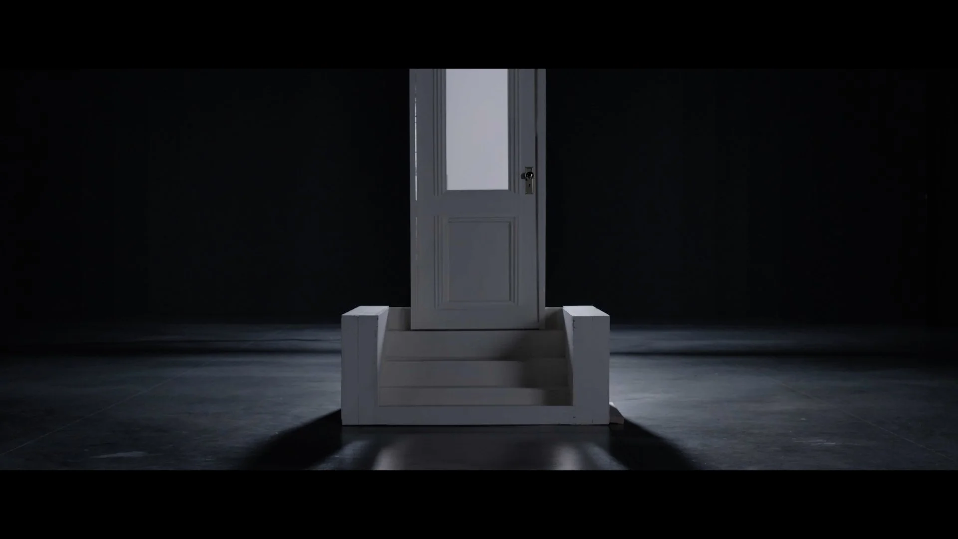 A white door with a glass panel, surrounded by darkness, with steps leading up to it in a dimly lit room.