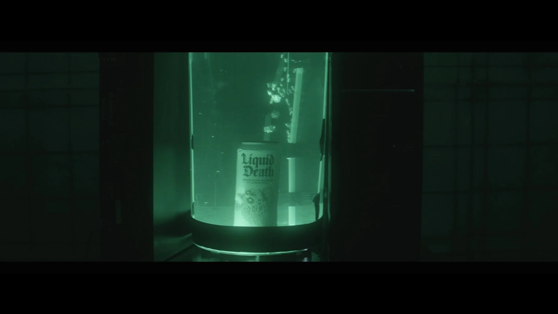 A glowing cylindrical container with green light, labeled 'Liquid Death' on a can inside, seen through the transparent surface.