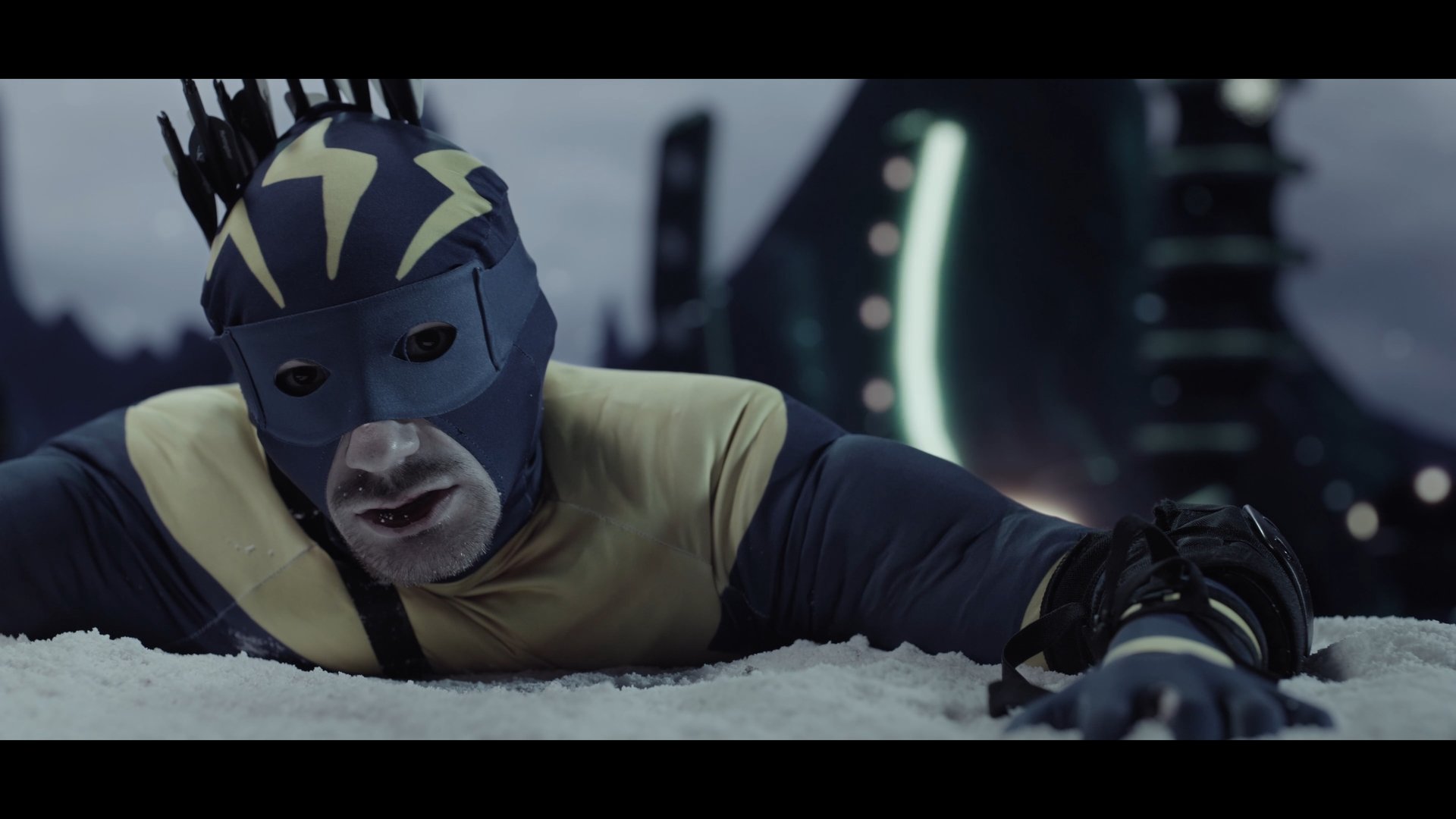 A man in a superhero costume lying on the snow, wearing a mask and a yellow and black outfit, with futuristic buildings in the background.