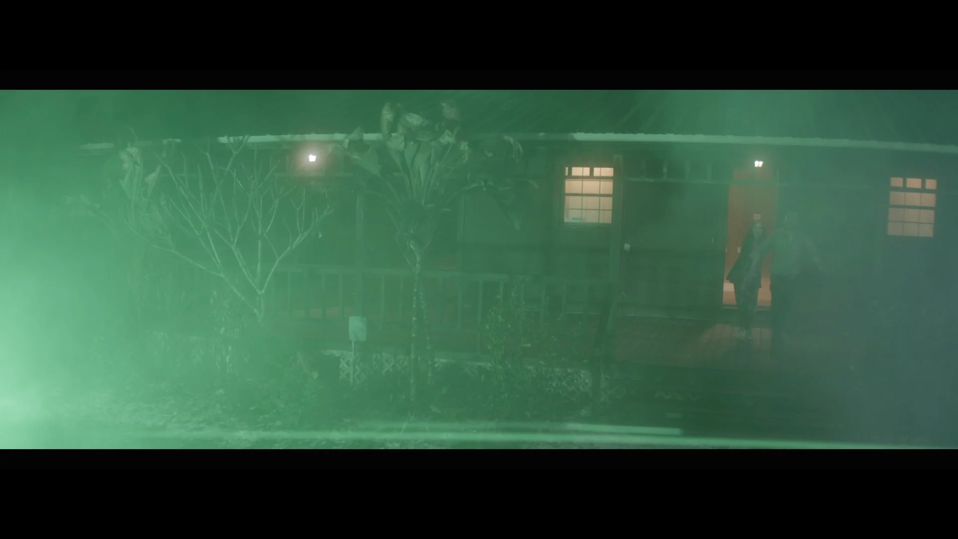 Nighttime scene of a house with two people standing on the porch.