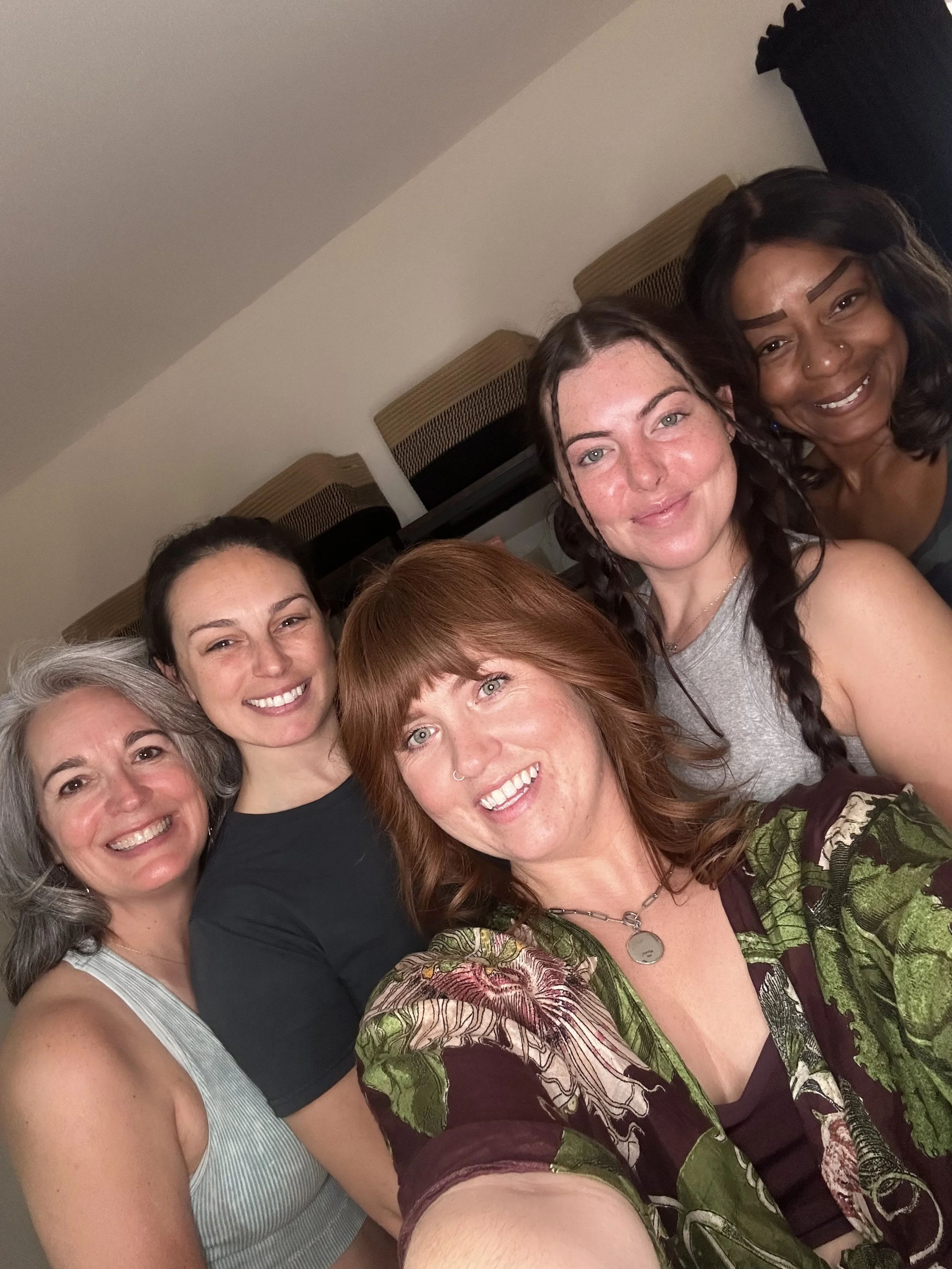 A group of several women smiling closely together for a selfie in an indoor setting.