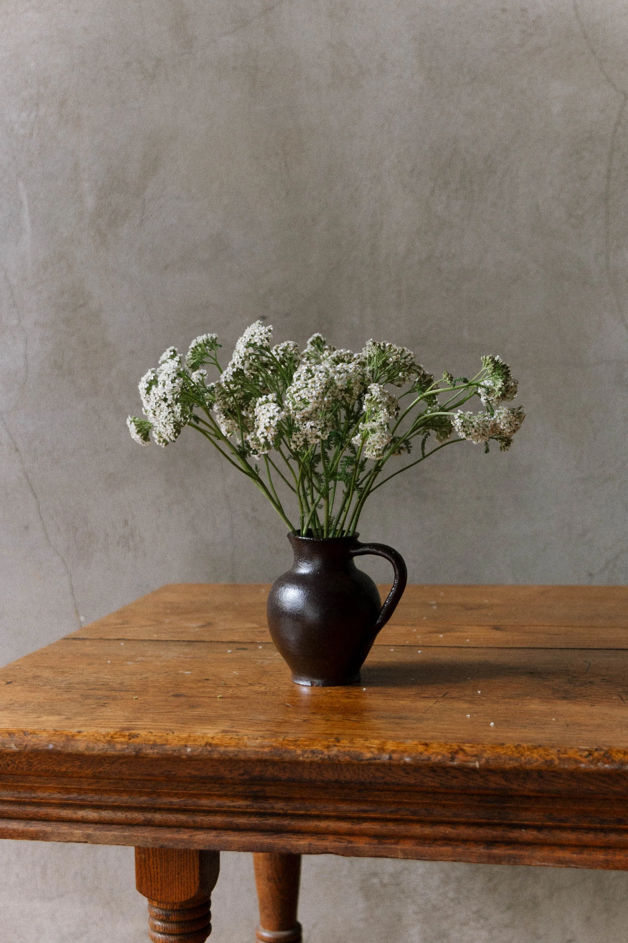 Vase with white yarrow flowers on a wooden table