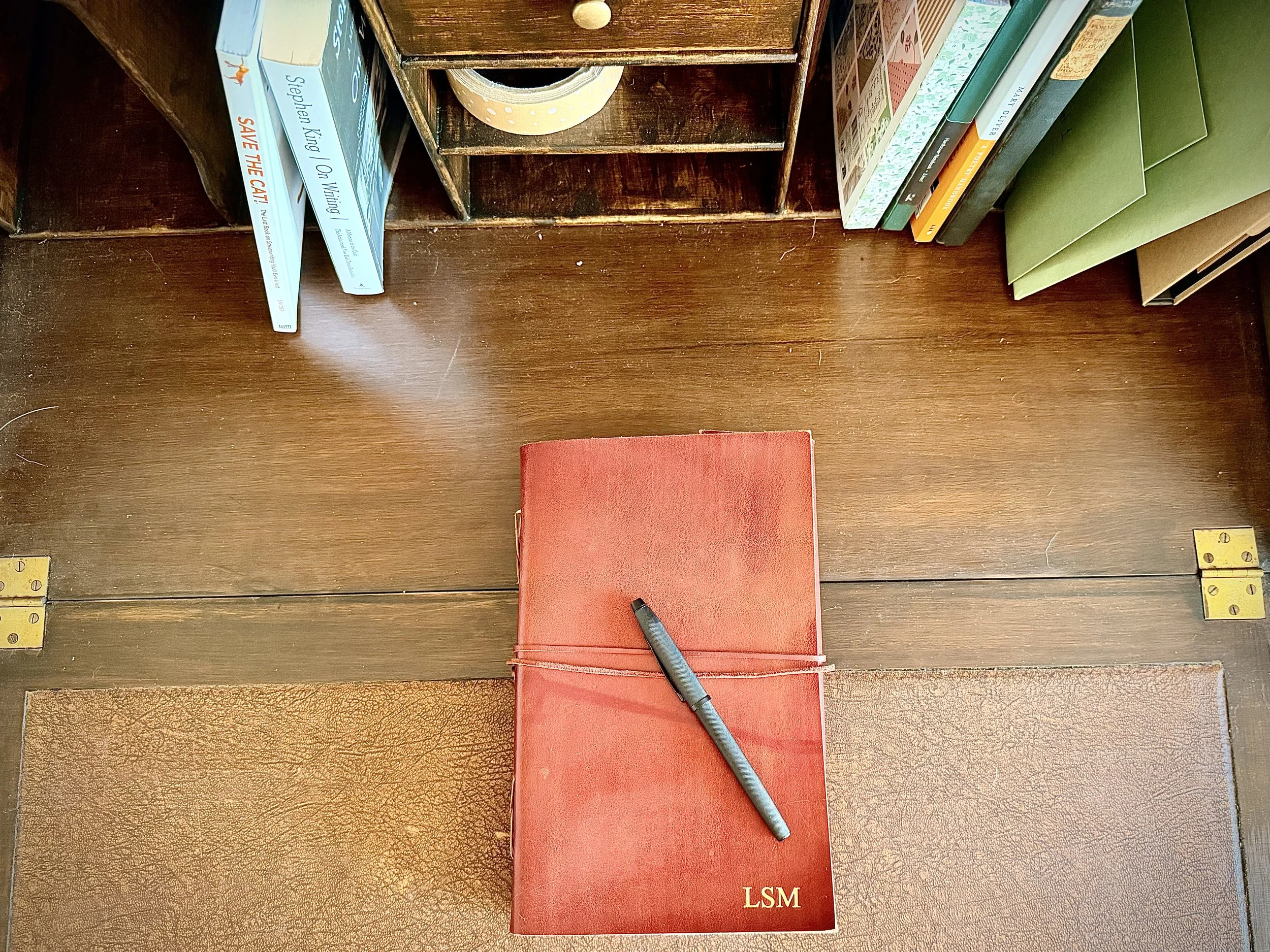 A wooden shelf with several books, a roll of yellow tape, and a black marker on top of a red notebook. The books are various colors and sizes, and some are leaning against the side of the shelf.