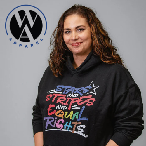 A woman with curly brown hair wearing a black hoodie with rainbow-colored text that says 'Stars and Stripes and Equal Rights.' She is standing in front of a light gray background with the Woke American Apparel logo.