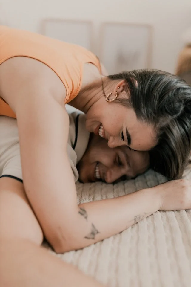 Two women sharing a joyful moment on a bed, embracing and smiling.