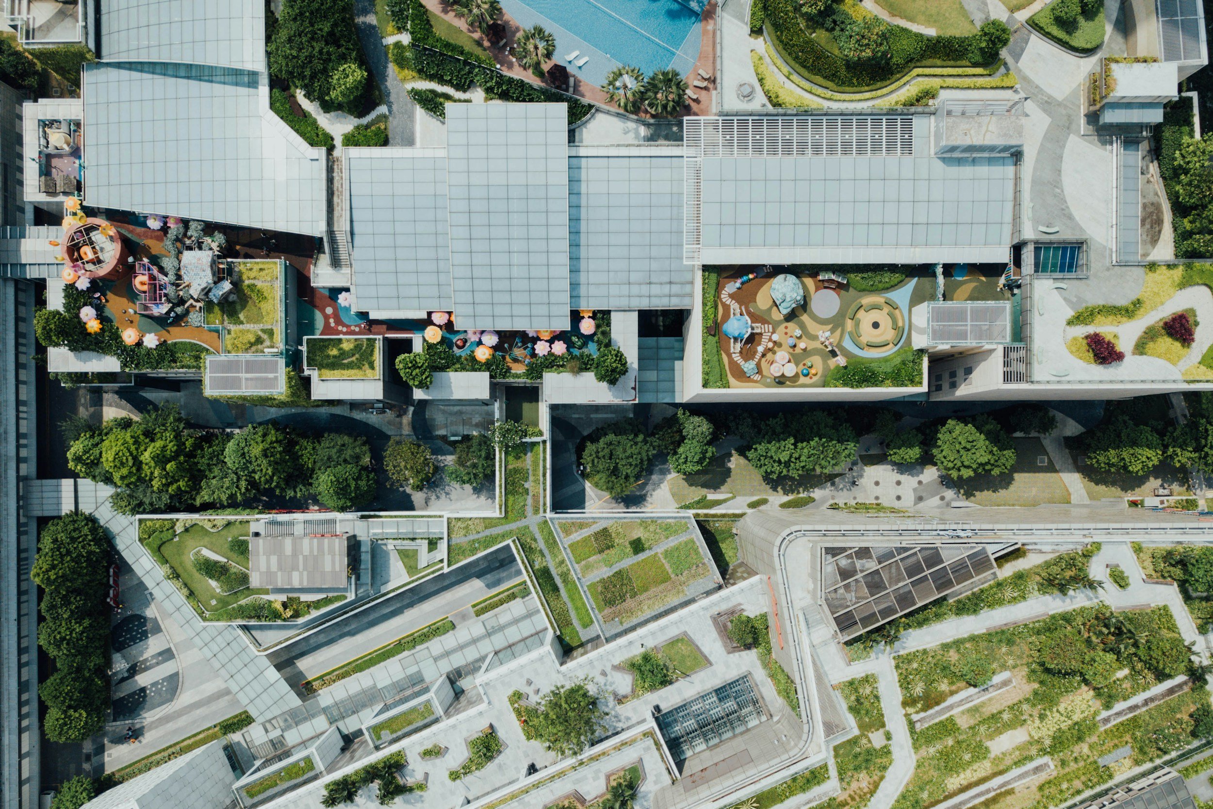 An aerial view of a modern urban rooftop garden with various green spaces, pathways, and recreational areas, surrounded by high-rise buildings.