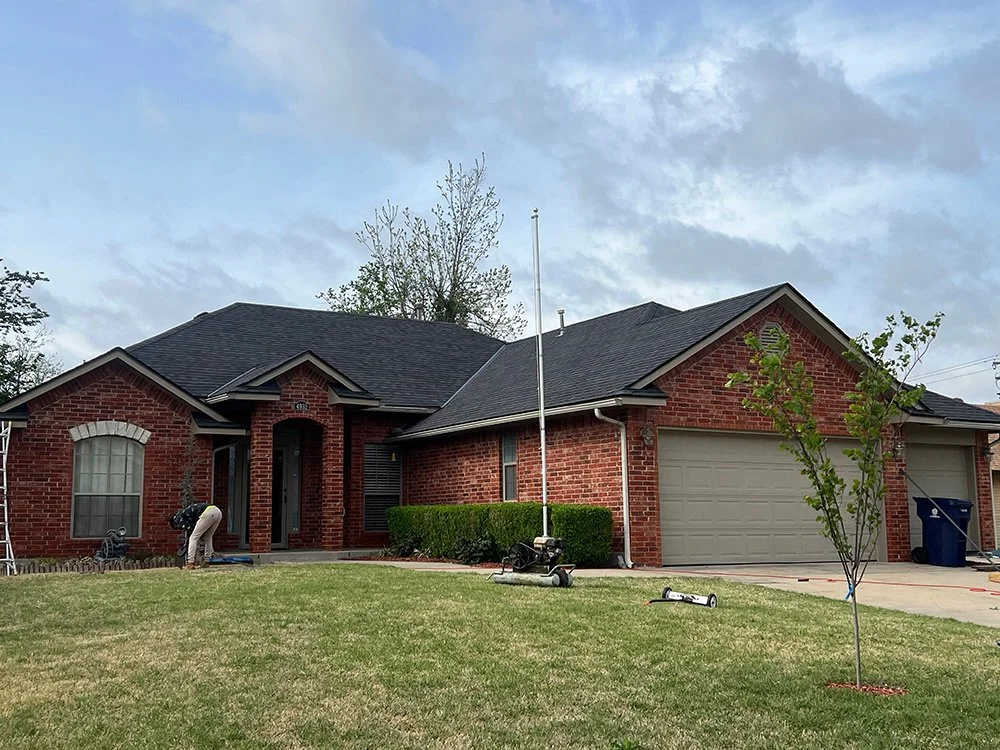 A brick house with a new roof, two windows, a garage, and a front lawn with a small tree
