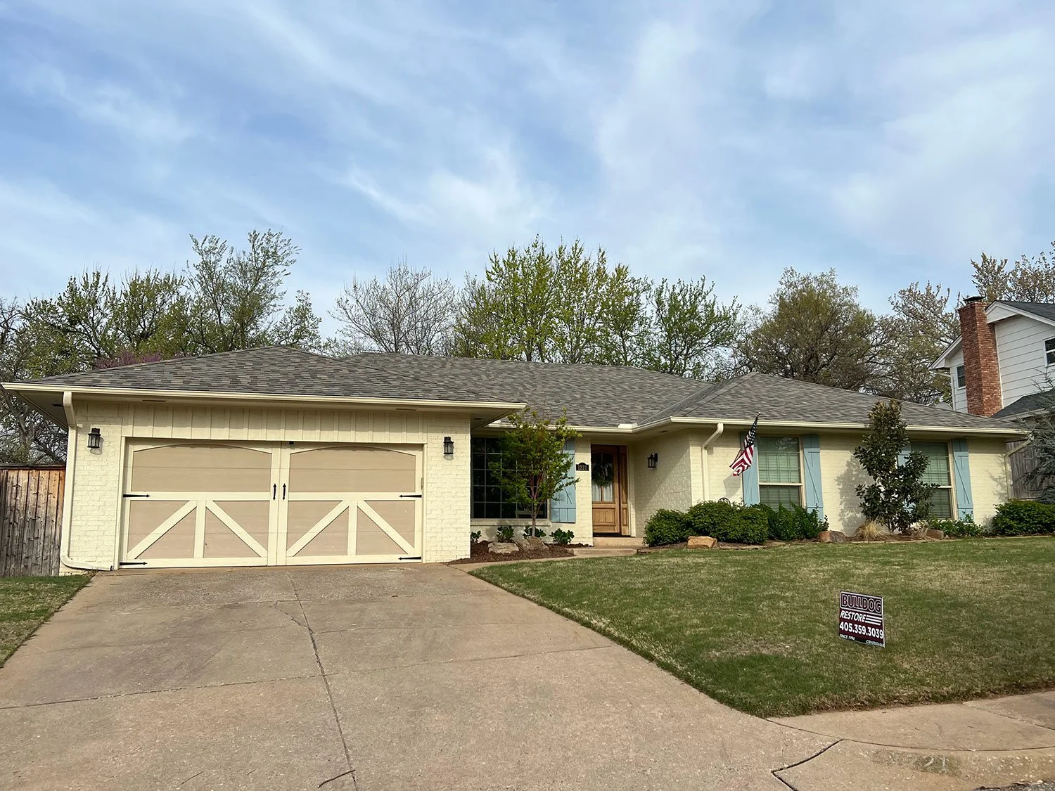 Single-story house with a new roof and a 'Bulldog Restoration' yard sign in the front yard.