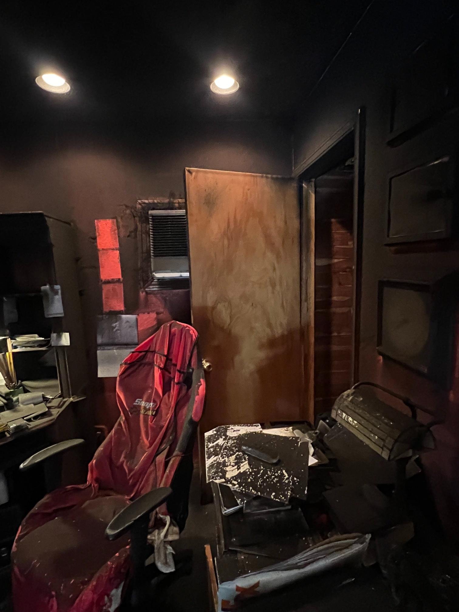 Dark office room with scattered items including a red backpack, black office chair, and a damaged desk.