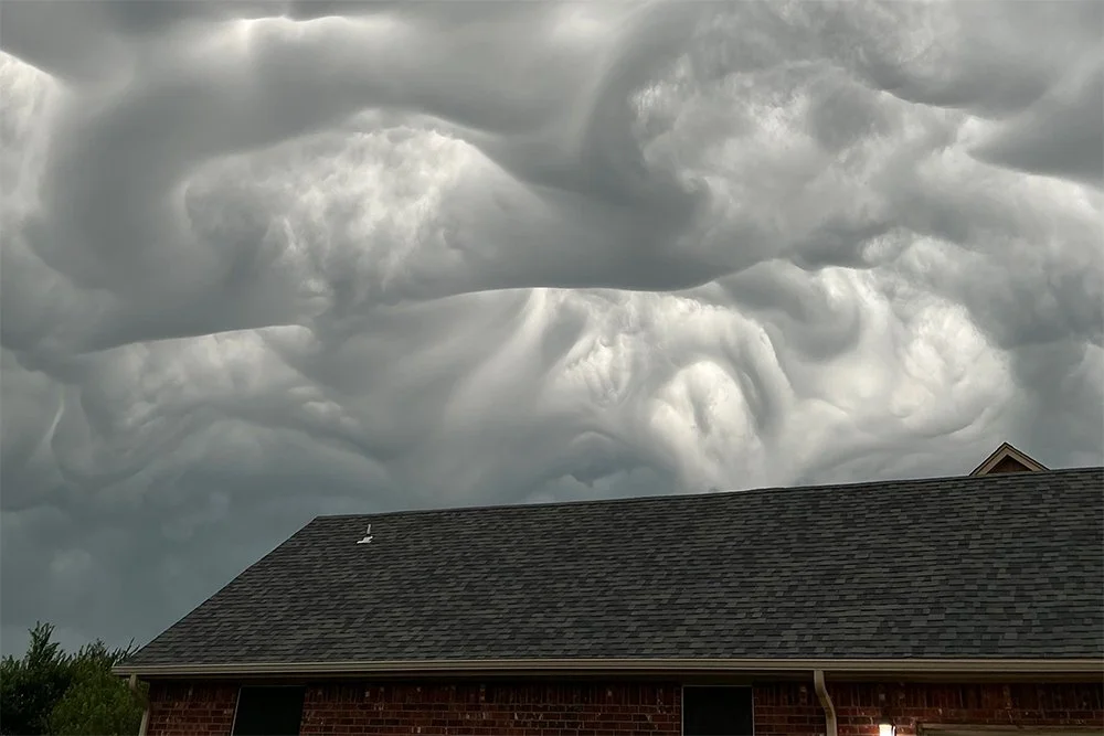 Dark, ominous storm clouds swirling over a house with a pitched roof.
