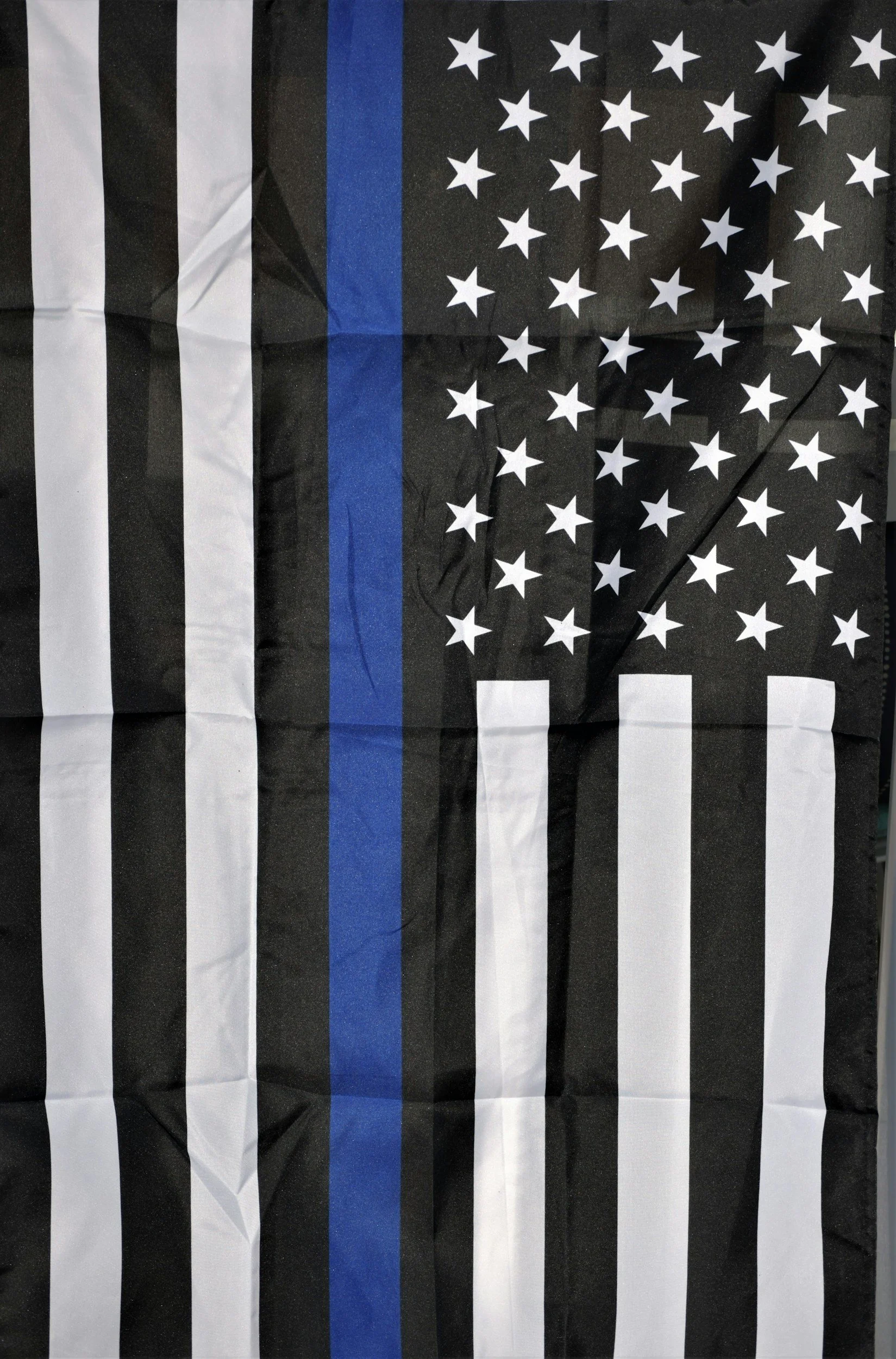 A wrinkled flag featuring black and white stripes, a black field with white stars, and a prominent blue stripe.