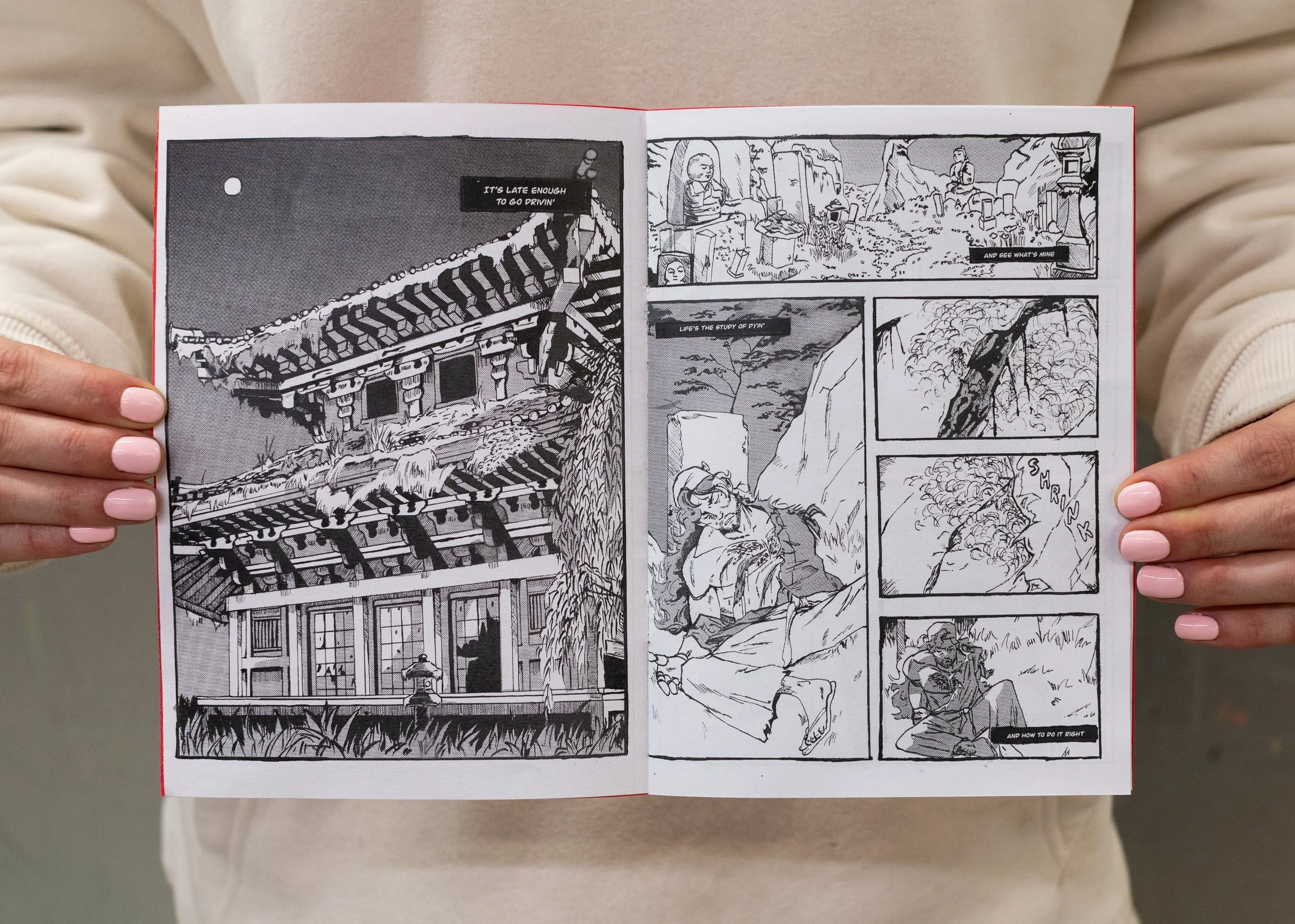 Person holding open spread of zine formatted black and white comic. Left page is a decrepit Shinto temple. Right page has four panels, the first is a Shinto cemetery, the second a man laying wounded against a headstone with three massive claw marks o
