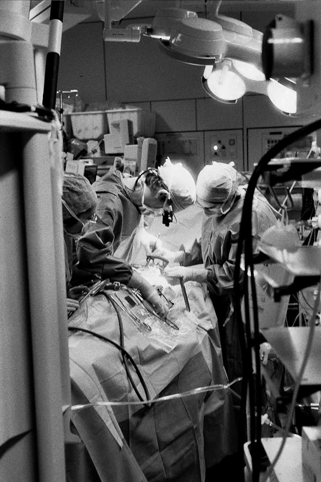 Team of surgeons performing an operation in an operating room with surgical lights overhead and medical equipment surrounding them.