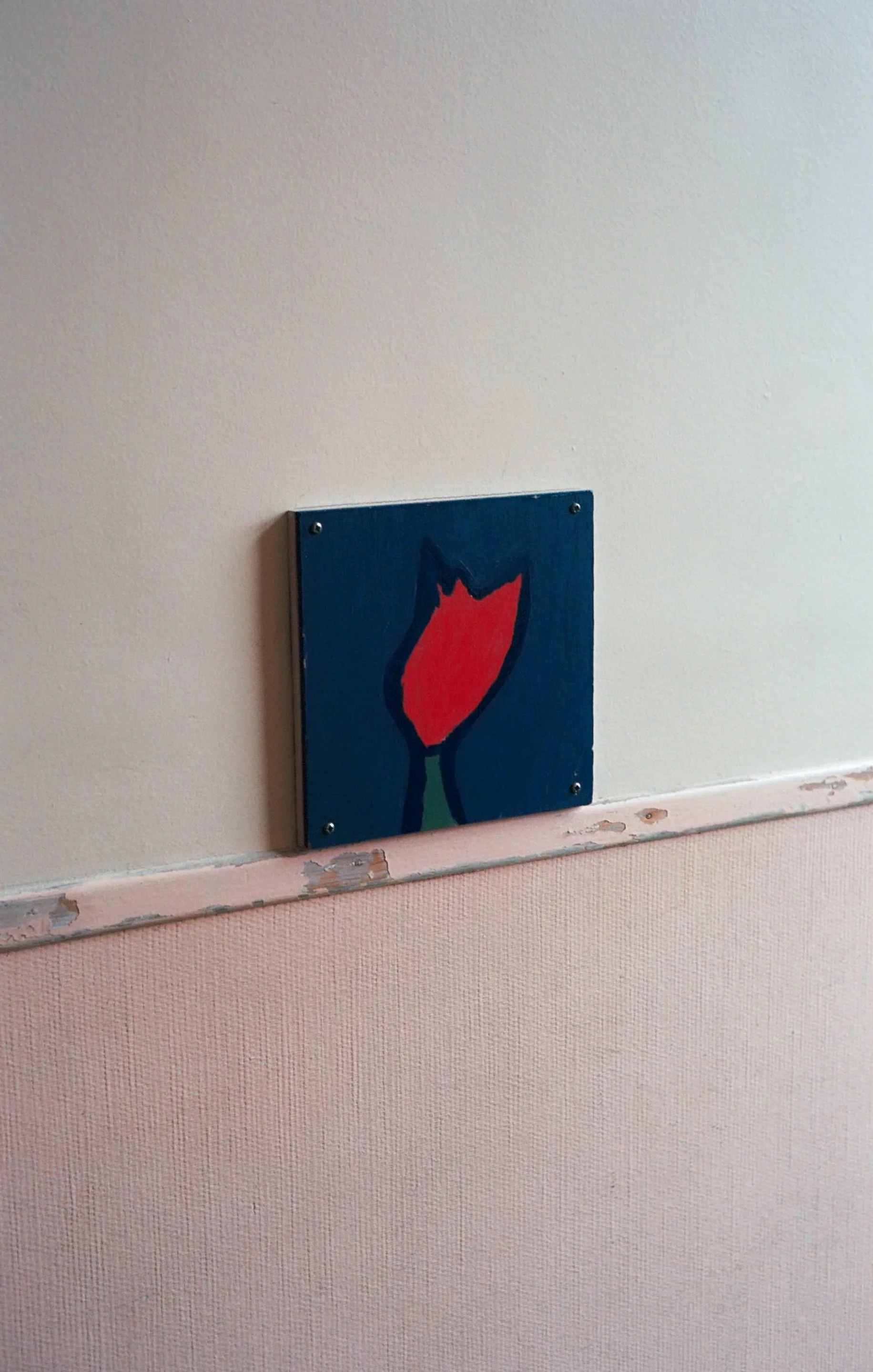 Wall with a small painting of a red tulip on a dark blue background.
