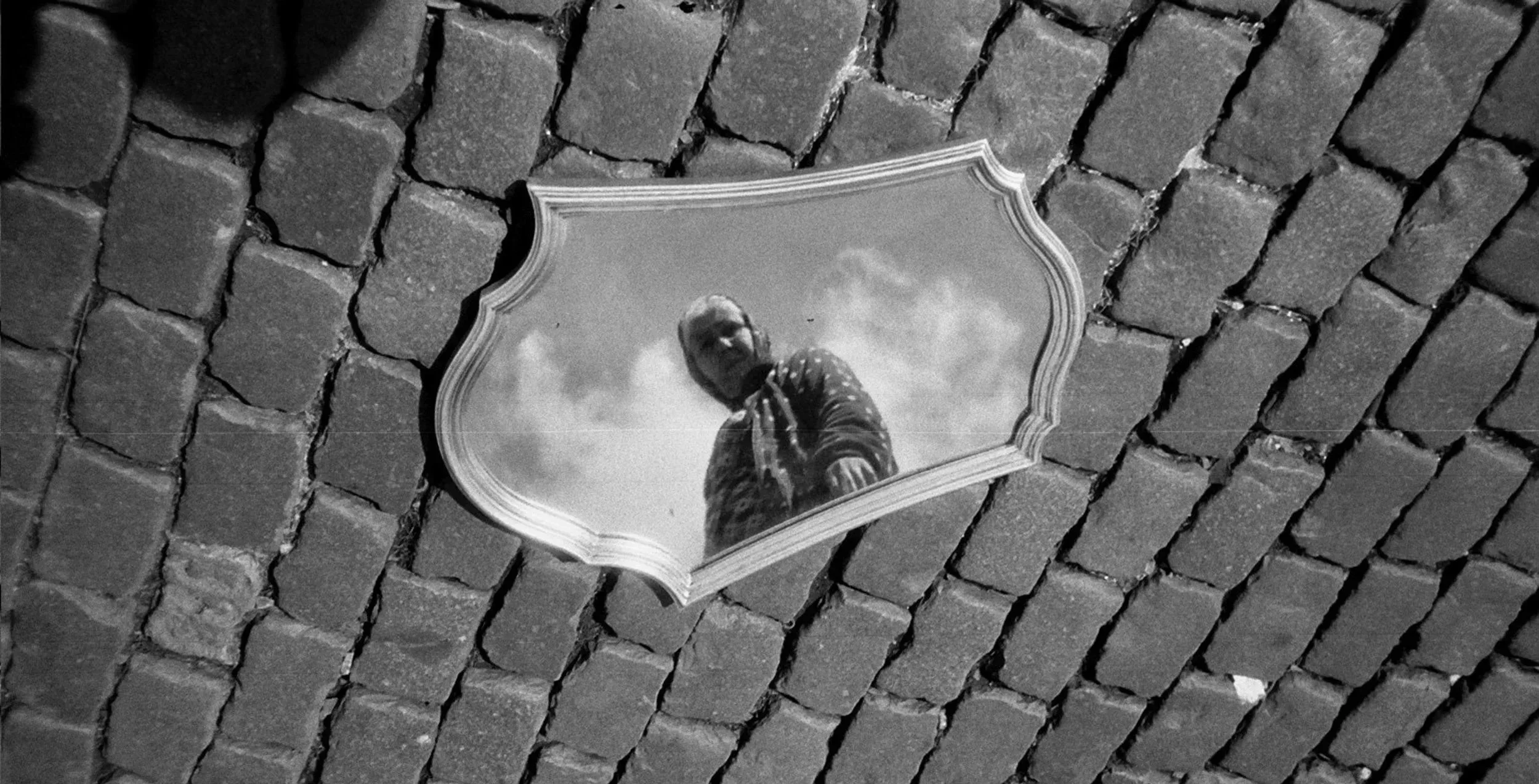 A mirror reflecting a person taking a photo, placed on a brick wall.