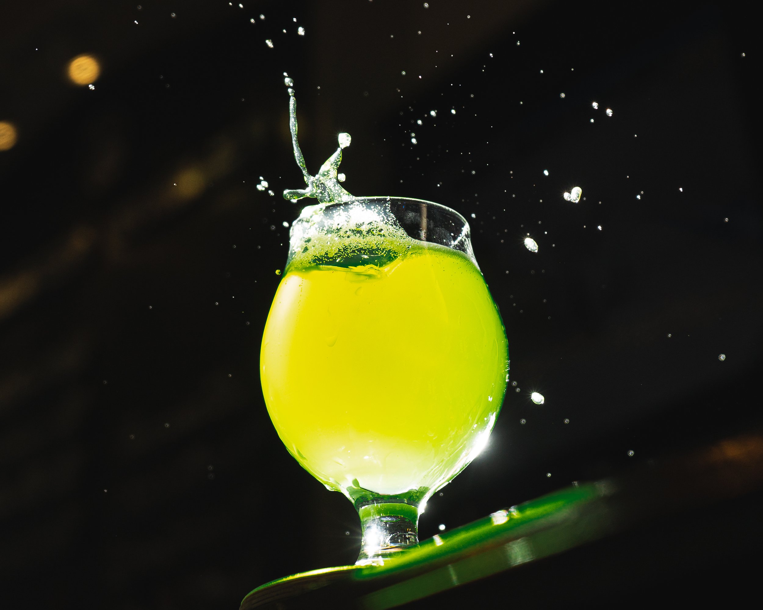 A splash of yellow-green liquid in a glass with a black background, with droplets flying around.