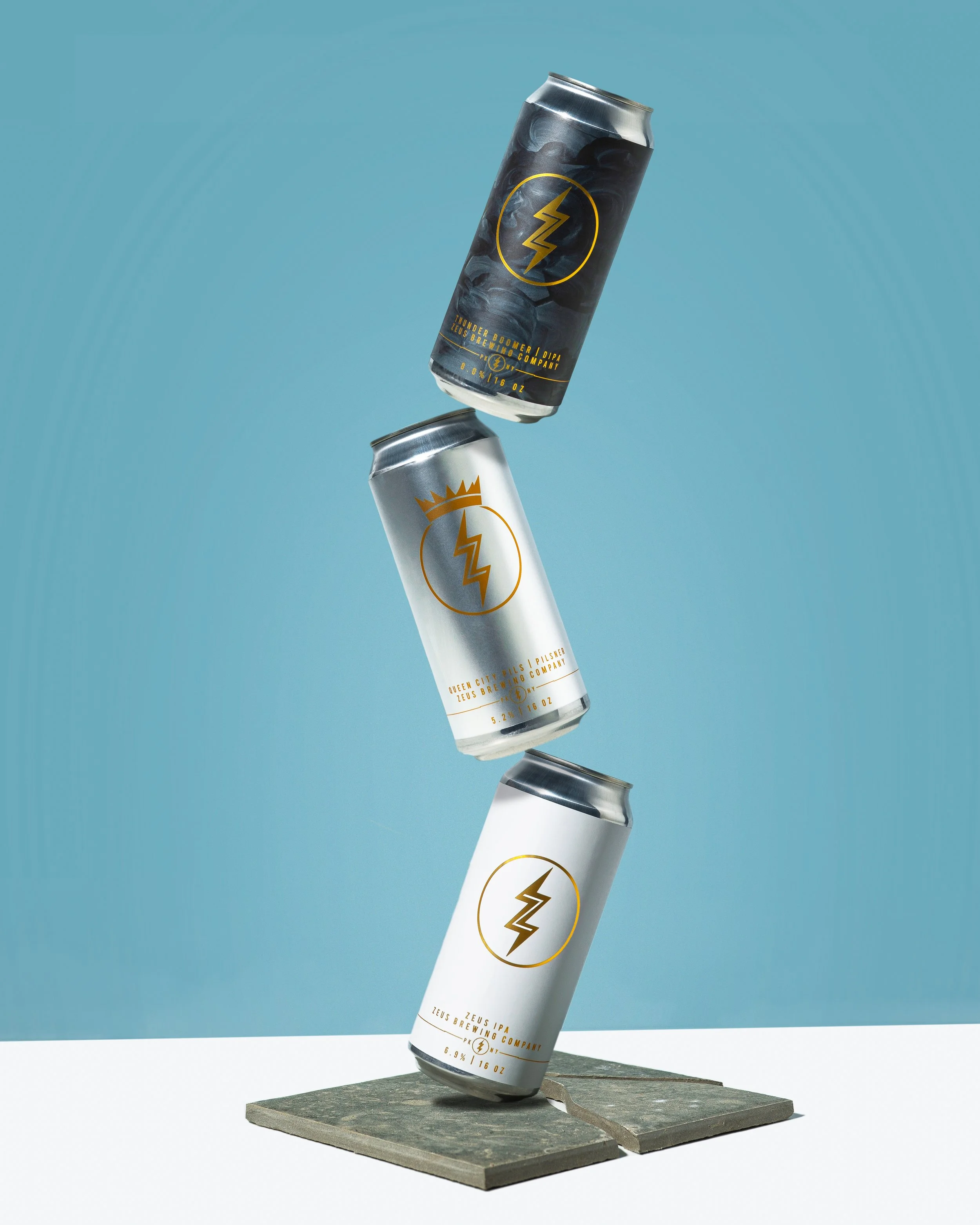 Three cans of Zeppelin beer stacked unevenly on a stone platform against a blue background.