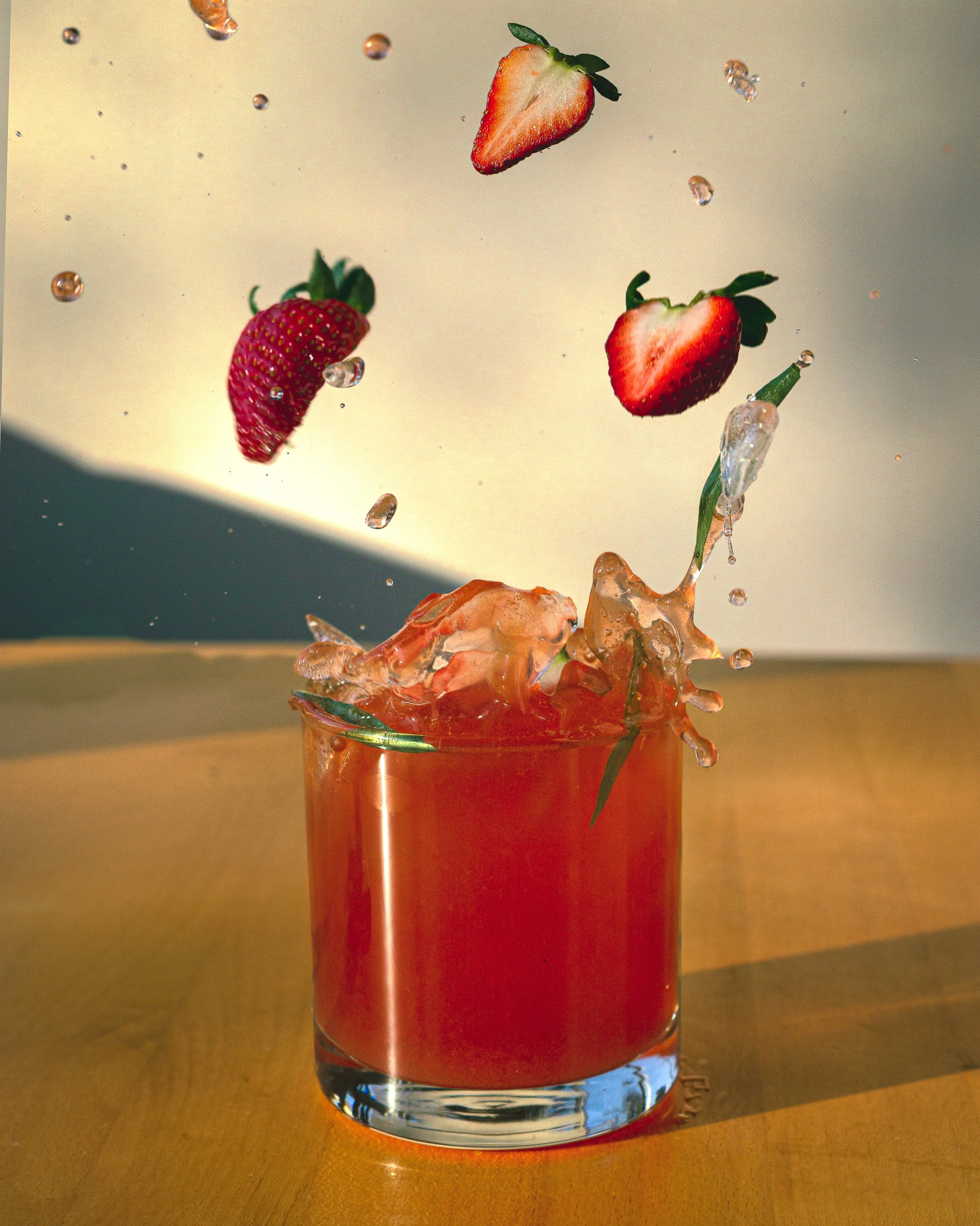 Fresh strawberries falling into a glass of red liquid with splashes and bubbles.
