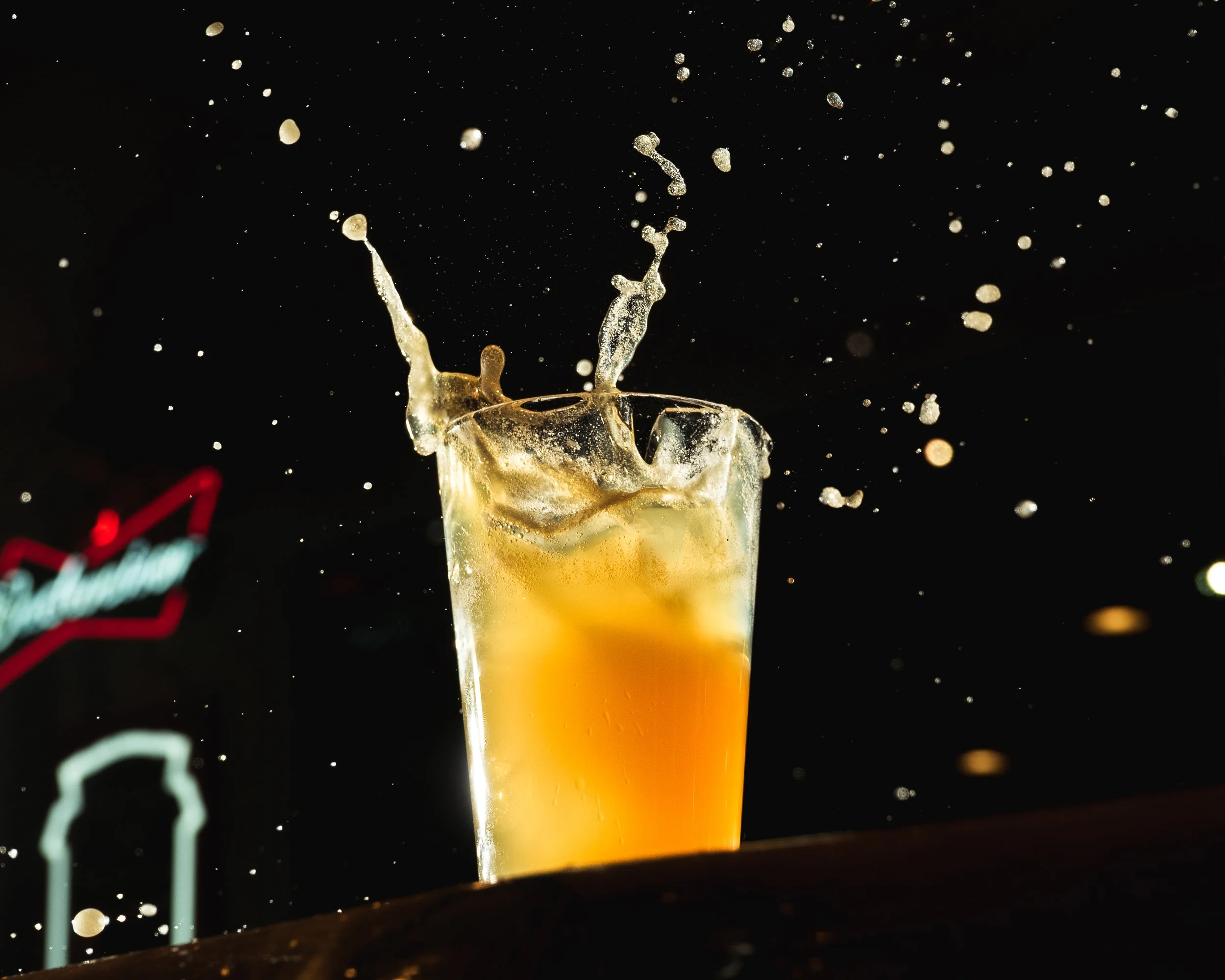 A glass of champagne with bubbles and splashes of liquid rising above it, set against a dark background.