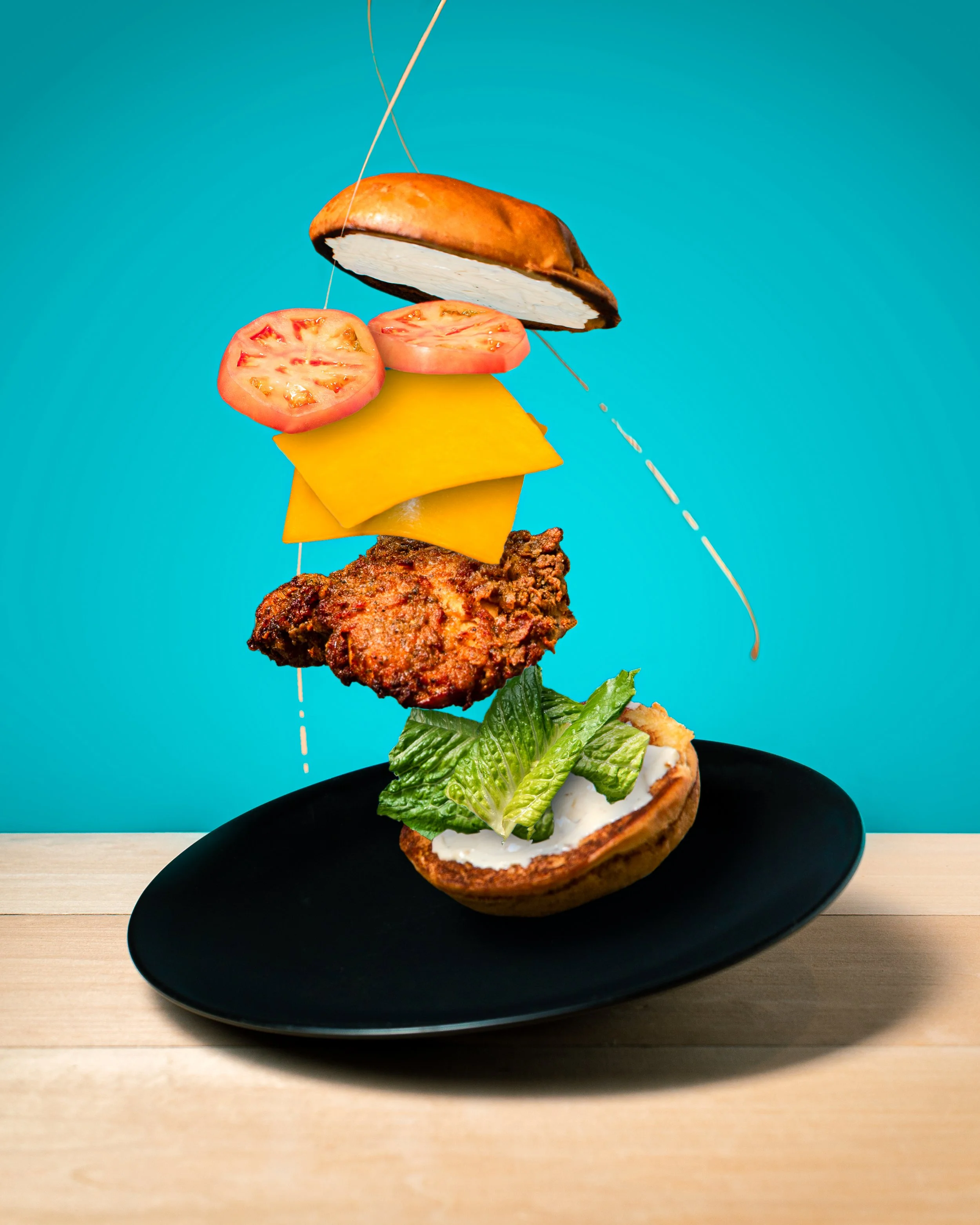 A novelty food sculpture mimicking a burger, with top bun, tomato slices, cheese, lettuce, and a bottom bun on a black plate.