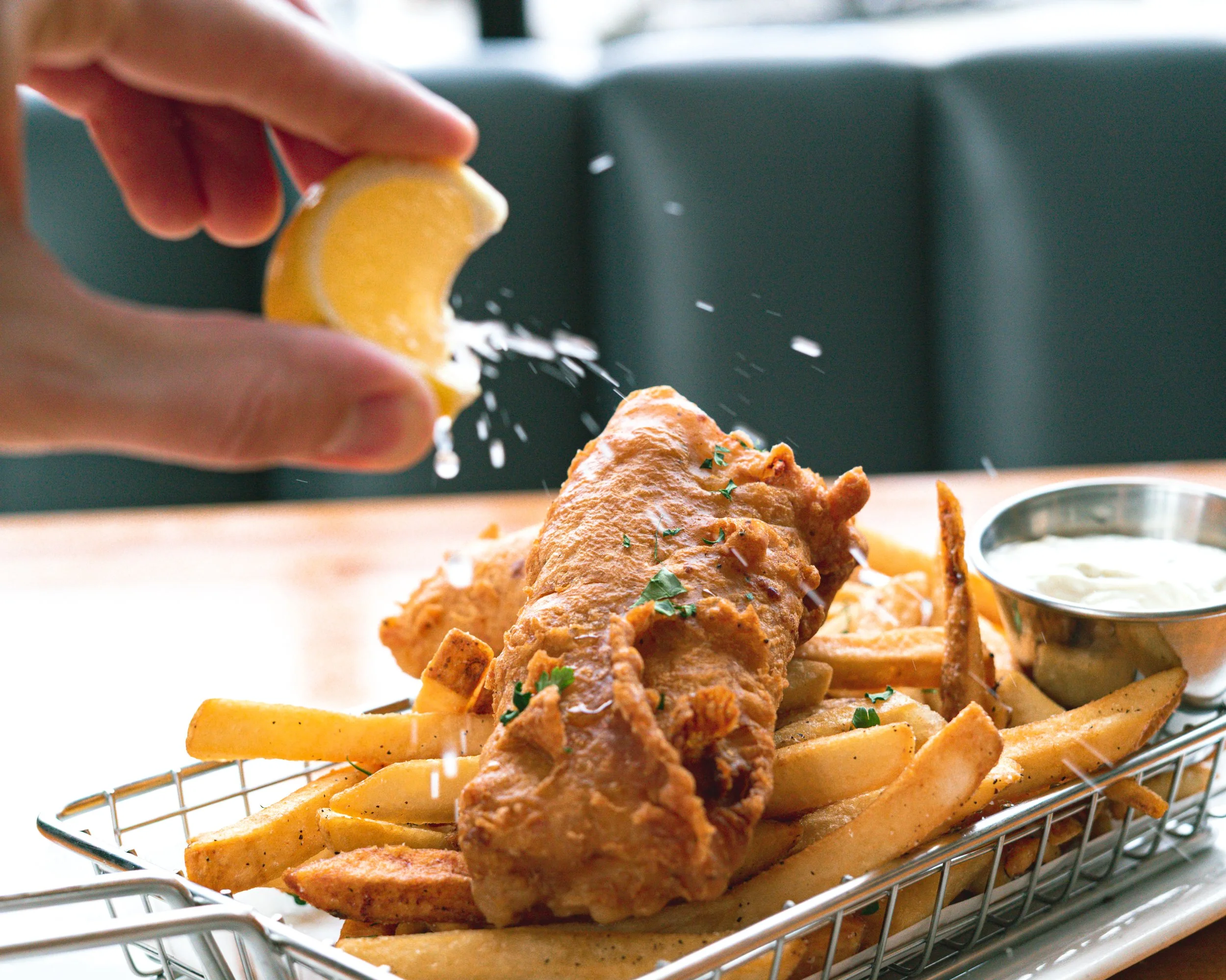 Close-up of crispy fried chicken on a toasted bun with lemon wedges, salt, and herbs, served on a metal wire rack.