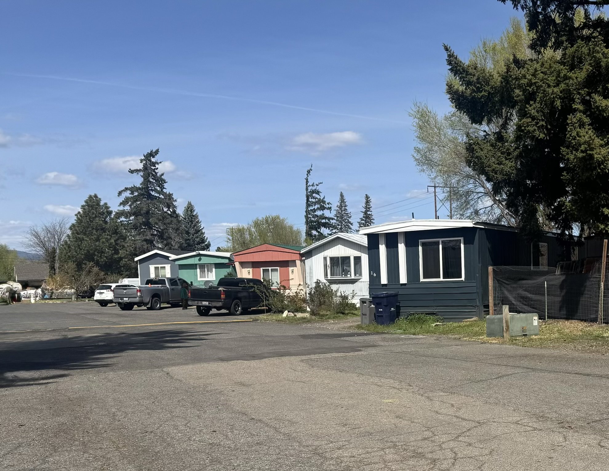 A small residential area with colorful single-story houses, parked trucks, and trees under a blue sky.