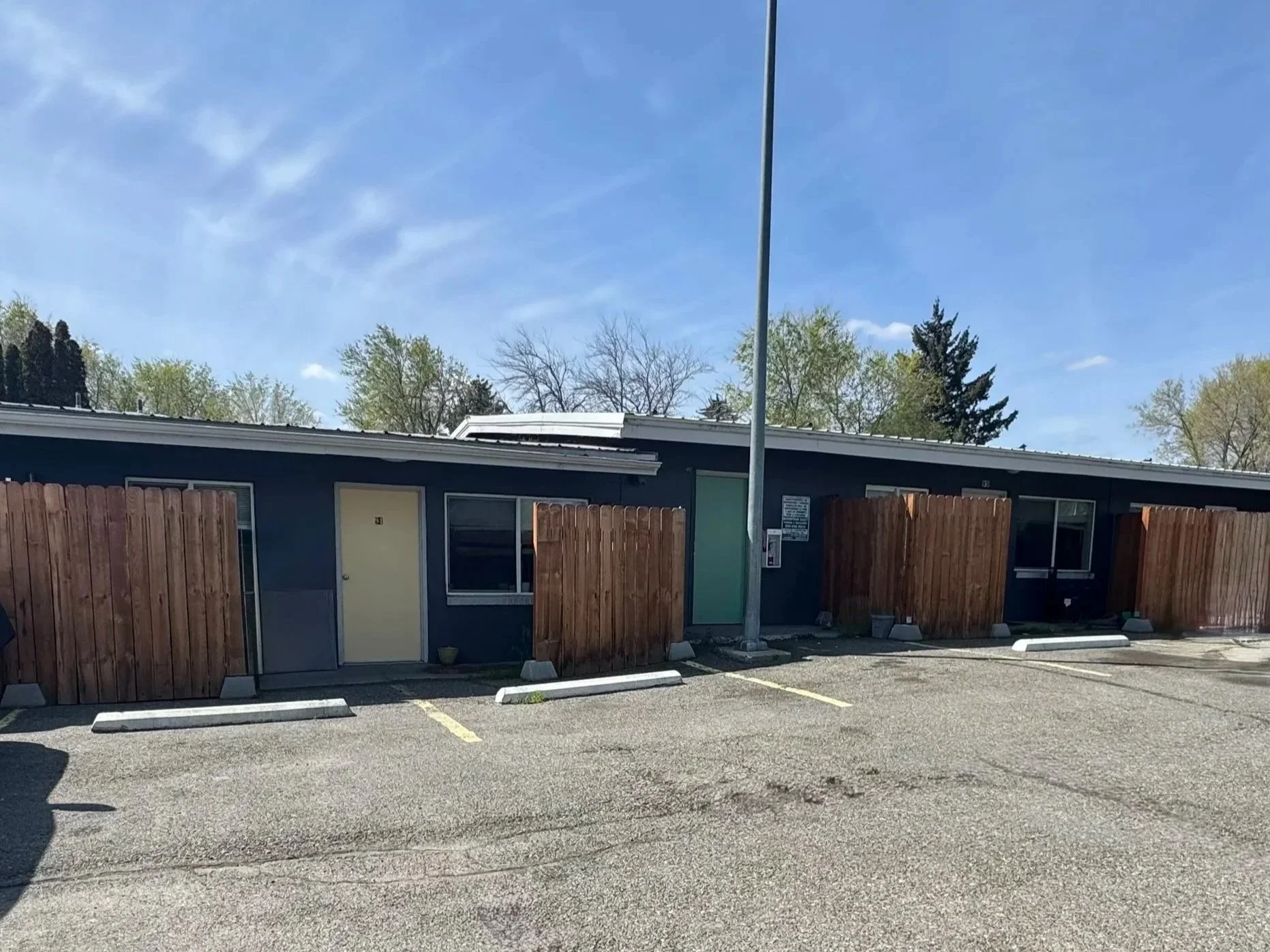 Single-story apartment building with seven units, wooden enclosed patios and parking spaces in front.