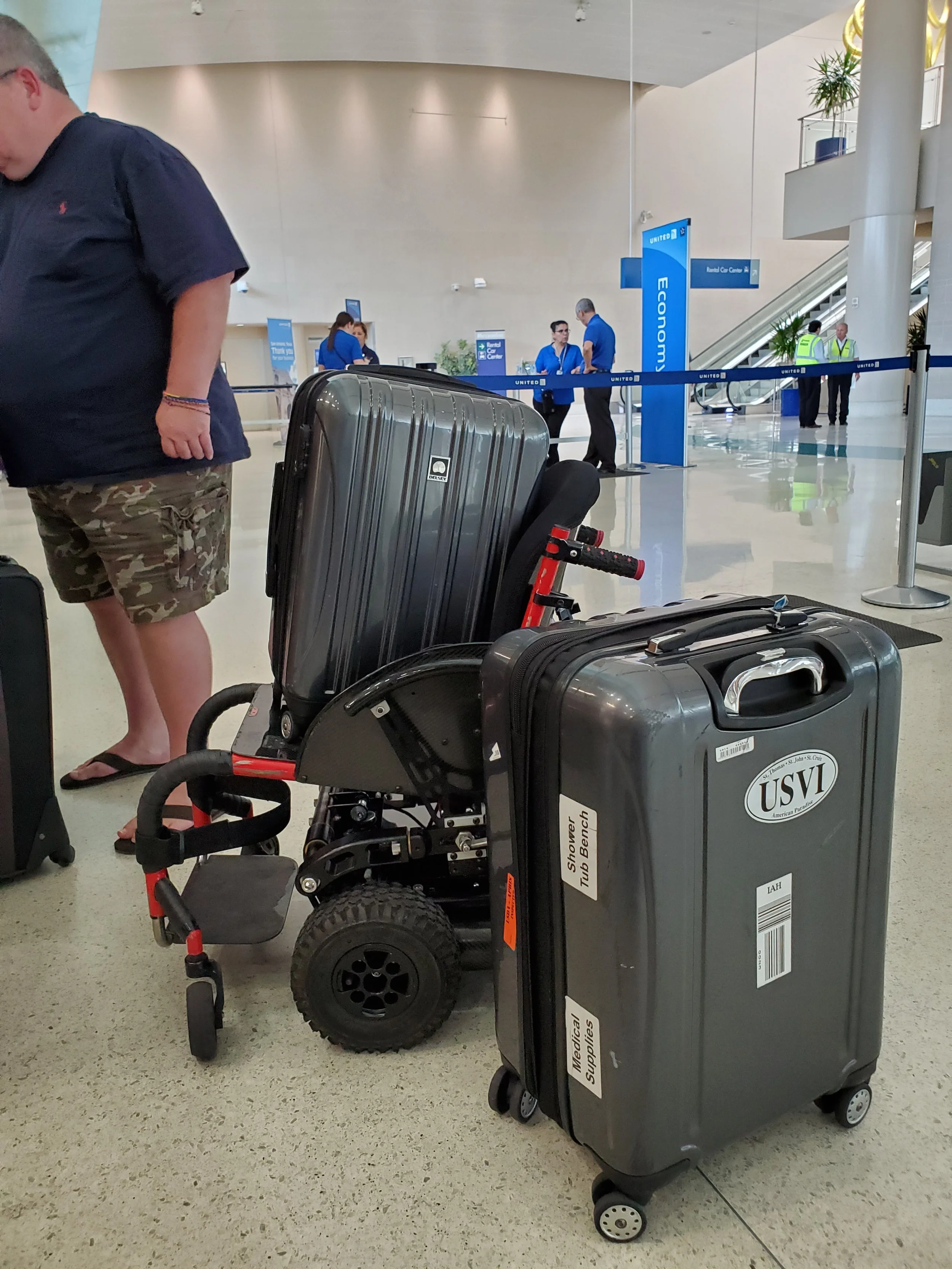 Luggage and a mobility aid at an airport baggage claim area with signs for United Airlines and a rental car center.