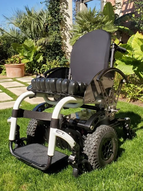 Electric wheelchair on a lawn with plants and a garden in the background.