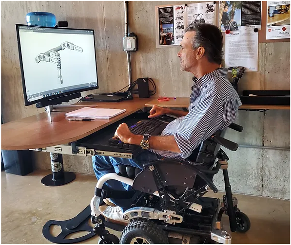 todd hargroder in his wheelchair working at a desk with a computer monitor displaying a 3D design of the power-flex