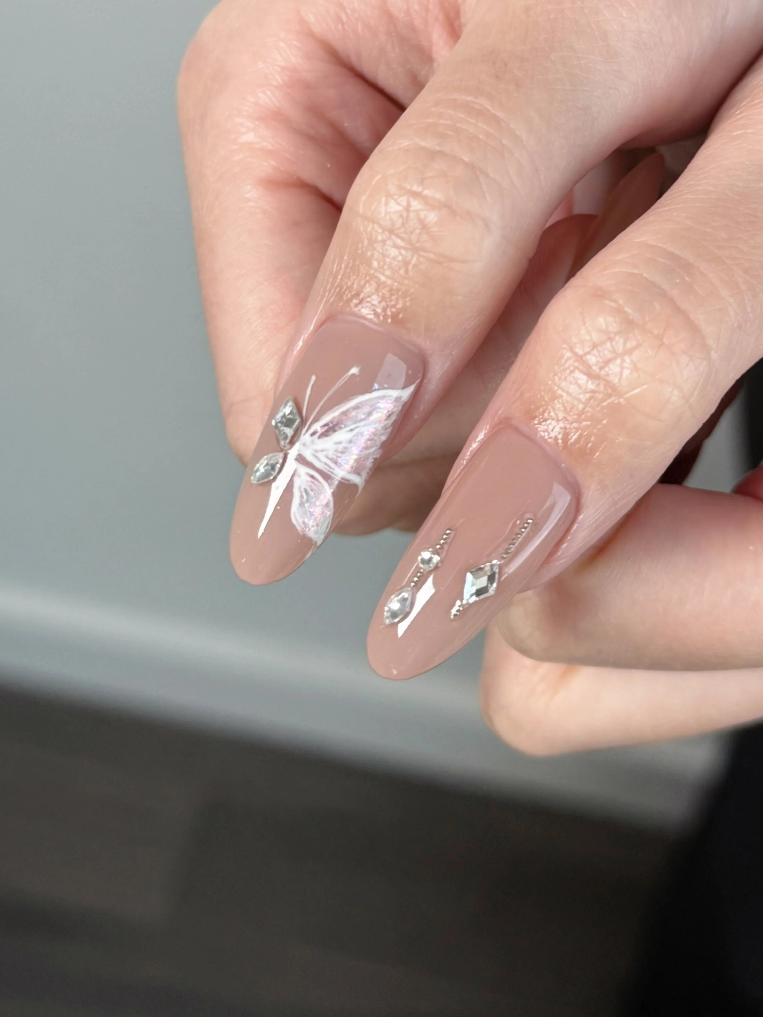 Nail art with a nude base, a white butterfly design, and rhinestone accents on the nails.