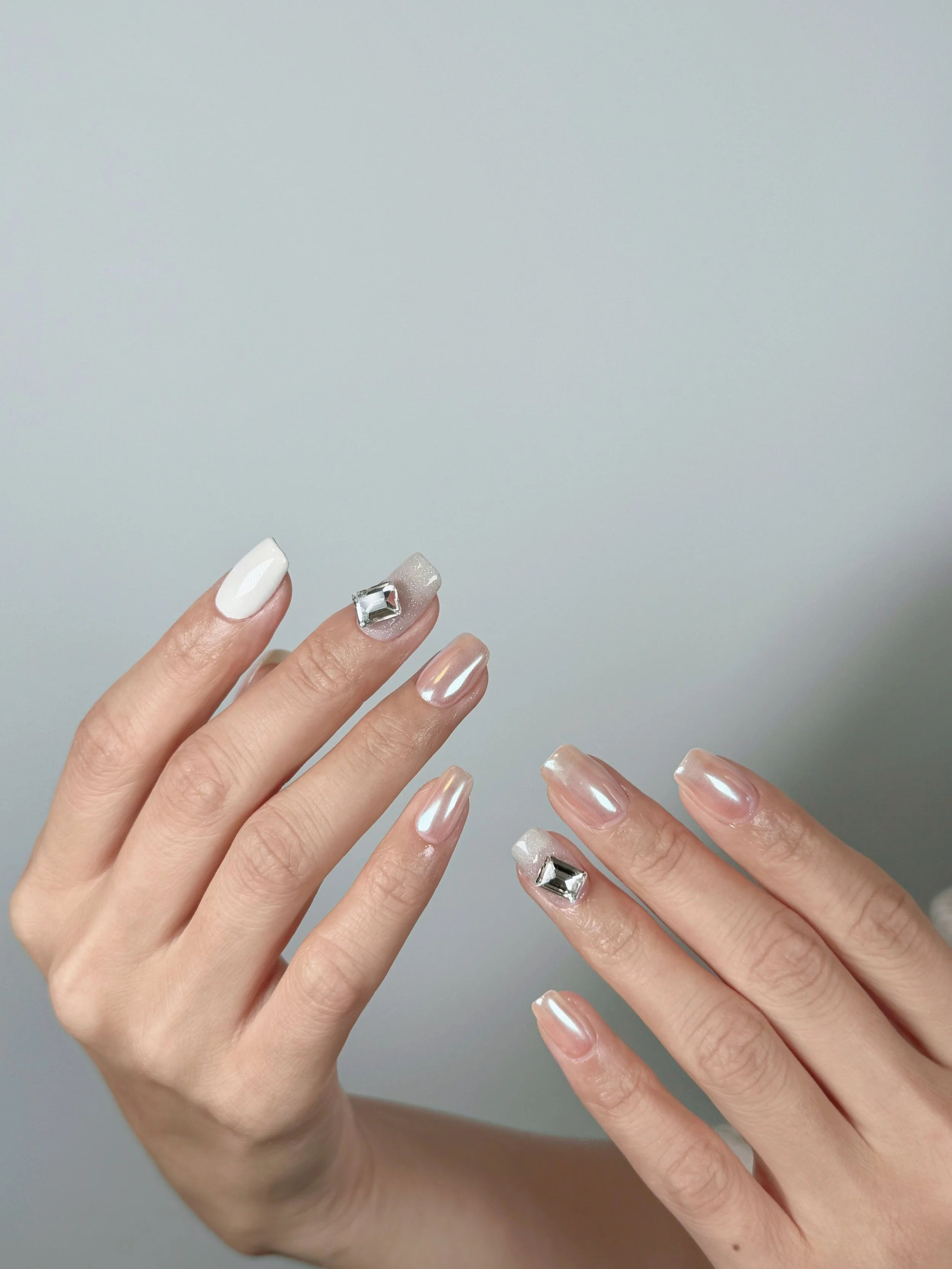 Close-up of a person's hands with manicured nails, featuring different designs, including pearls, metallic, glitter, and gemstone accents.