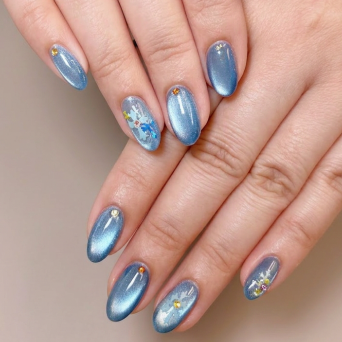 Manicure nails painted with shimmery blue nail polish, decorated with small gold and yellow rhinestones and tiny decorative designs.