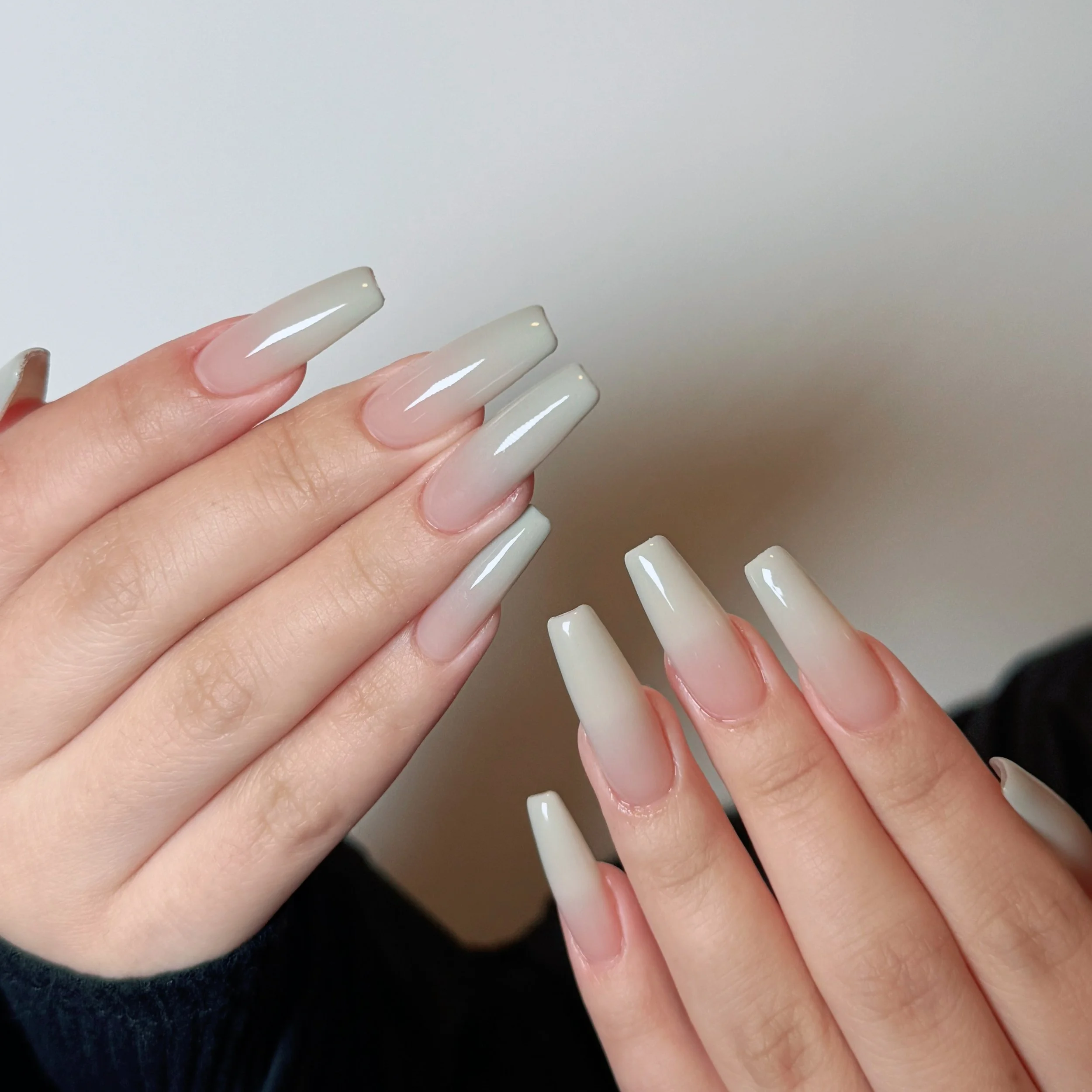 Close-up of a person's hands with long, square-shaped acrylic nails painted in a glossy, ombre white-to-clear gradient.