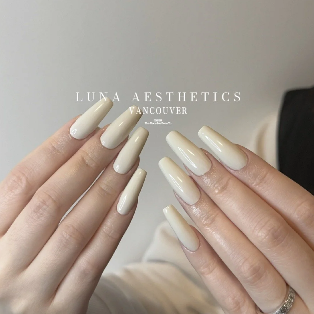 Close-up of manicured hands with long, cream-colored, glossy acrylic nails. Text overlay reads "LUNA AESTHETICS VANCOUVER."