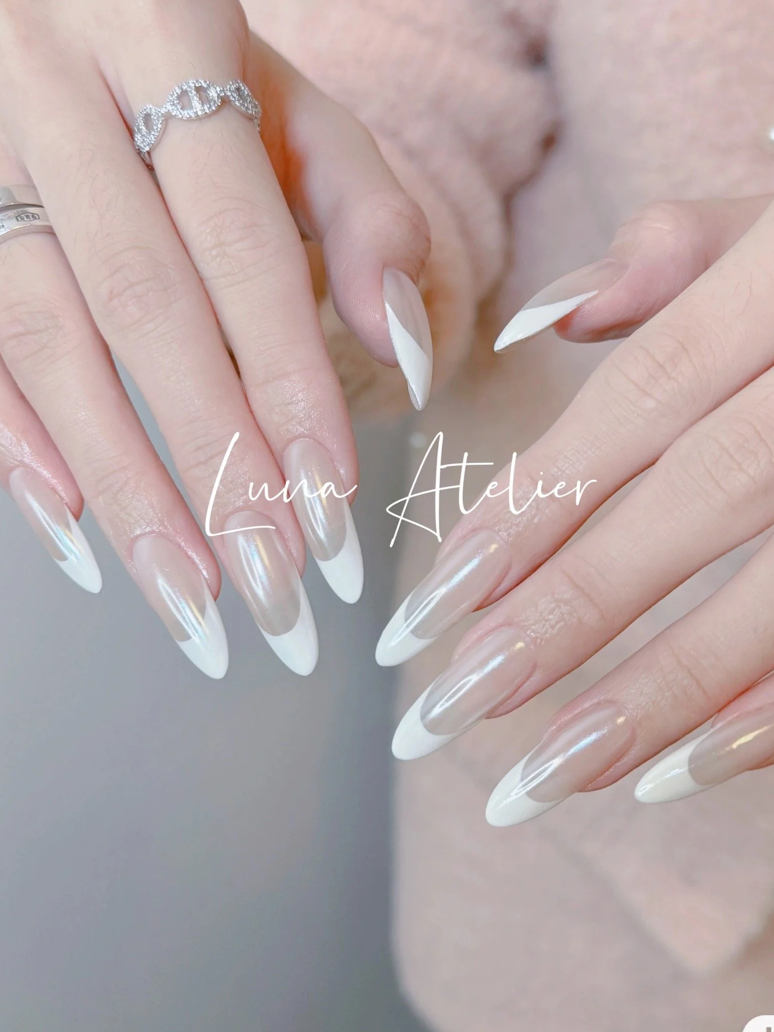 Close-up of hands showing french nail art with long white and clear nails, one hand has a silver DNA double helix ring, The text over the image reads 'Luna Atelier'.