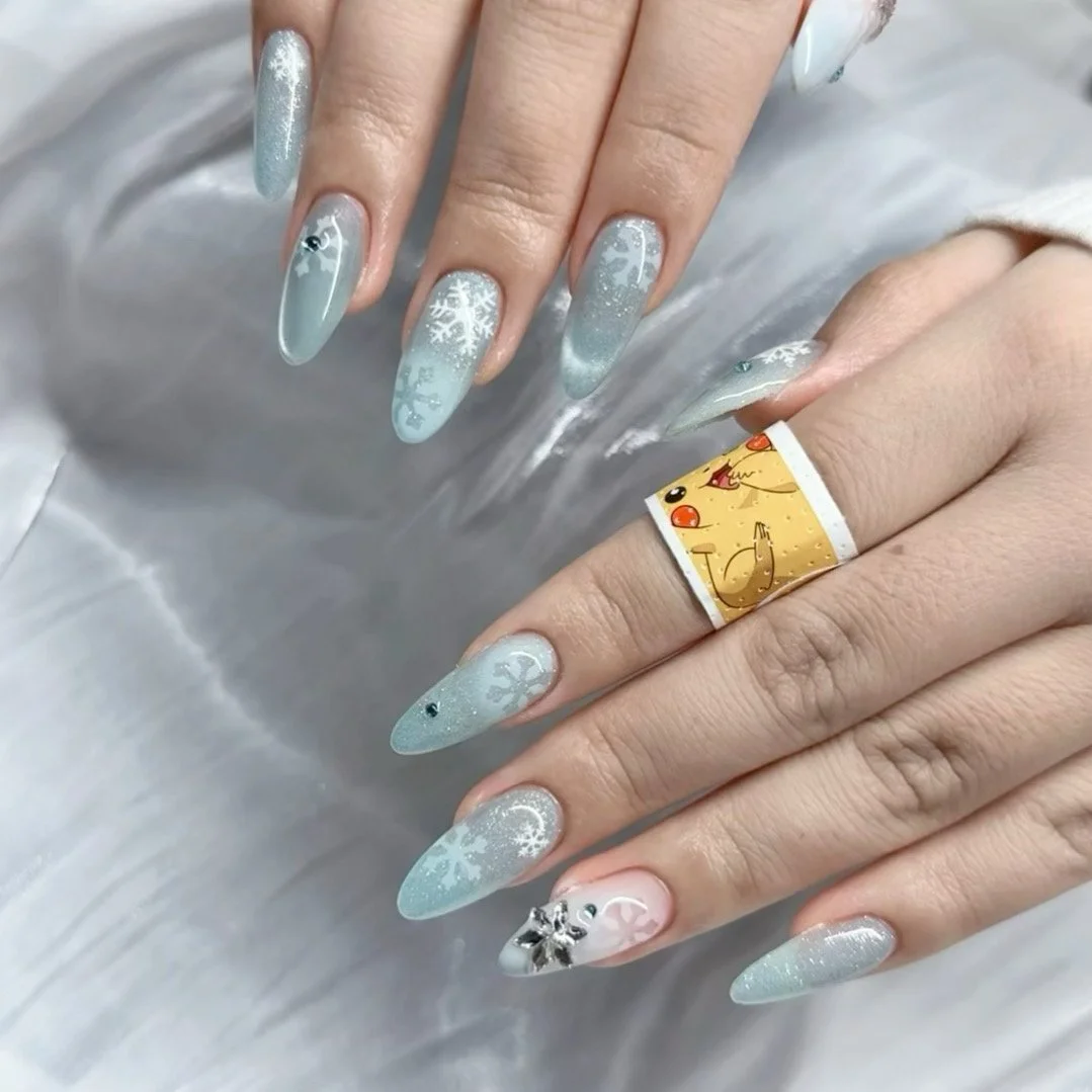 Close-up of a hand with decorated winter-themed nail art featuring snowflakes and icy silver designs, wearing a ring with a cartoon snowman.