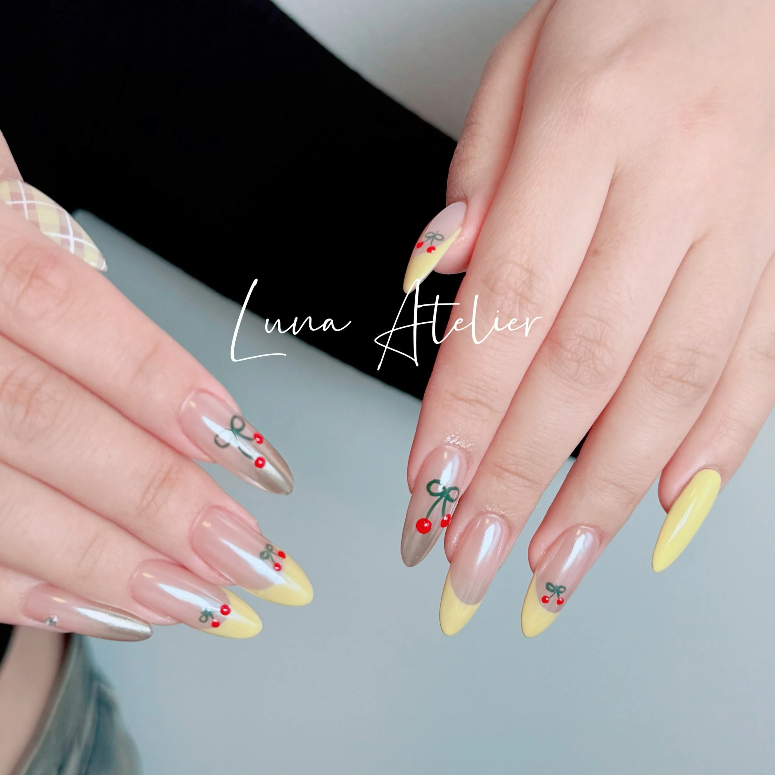 Manicured nails with Christmas-themed nail art, including bows and red berries, on natural and yellow-colored nails, with the text 'Luna Atelier' overlayed.