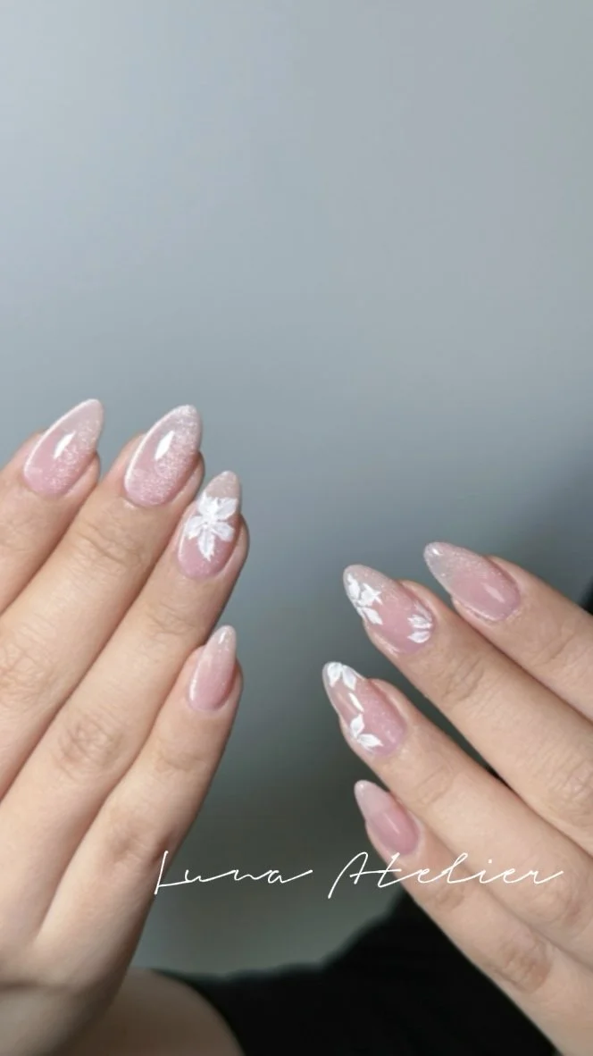 Nail art with light pink base and white floral designs on the ring fingers. The nails are almond-shaped and glossy.