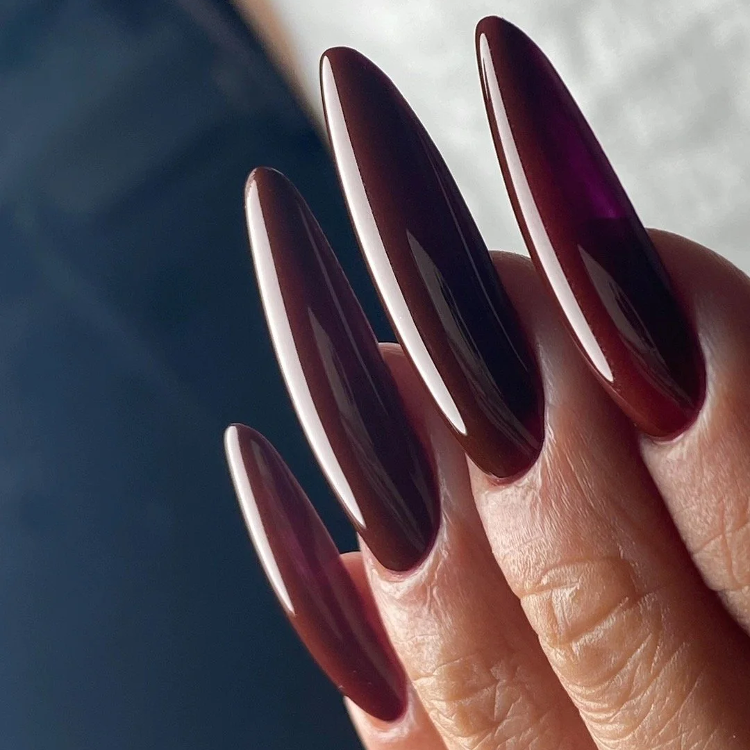 Close-up of long, oval-shaped nails painted in a deep, glossy burgundy color on a person's hand.