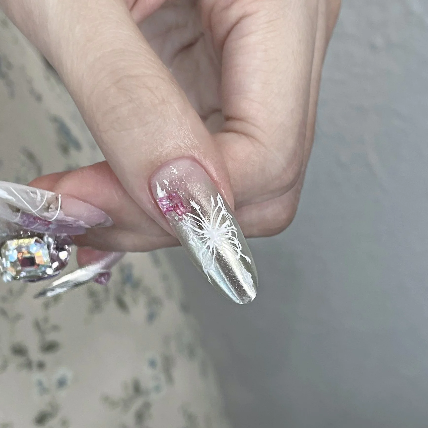 Close-up of a hand showing an acrylic nail with a white butterfly design, pink accents, and rhinestones.