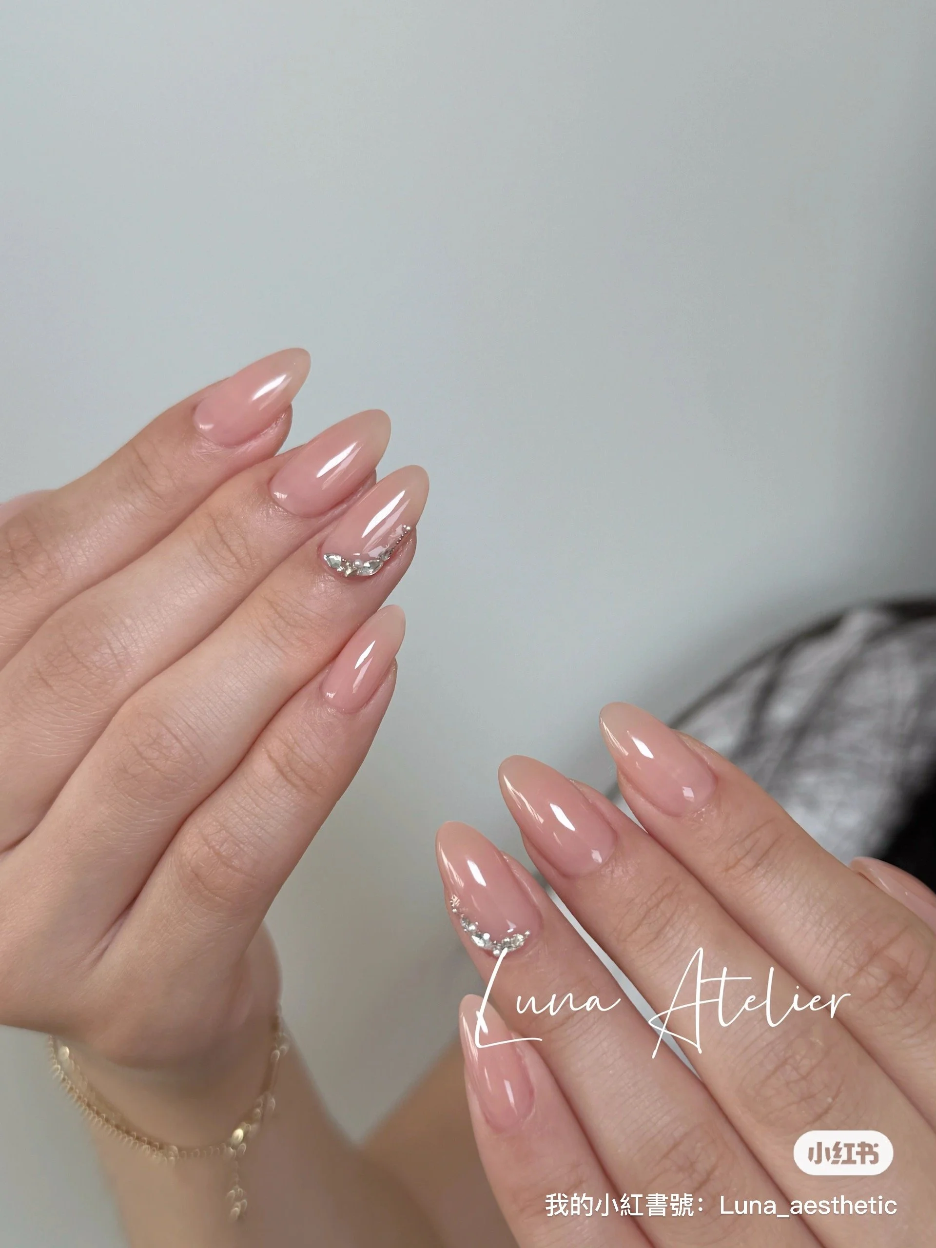 Close-up of a woman's hands showing a fresh, nude-colored manicure with silver rhinestones on the ring fingers.