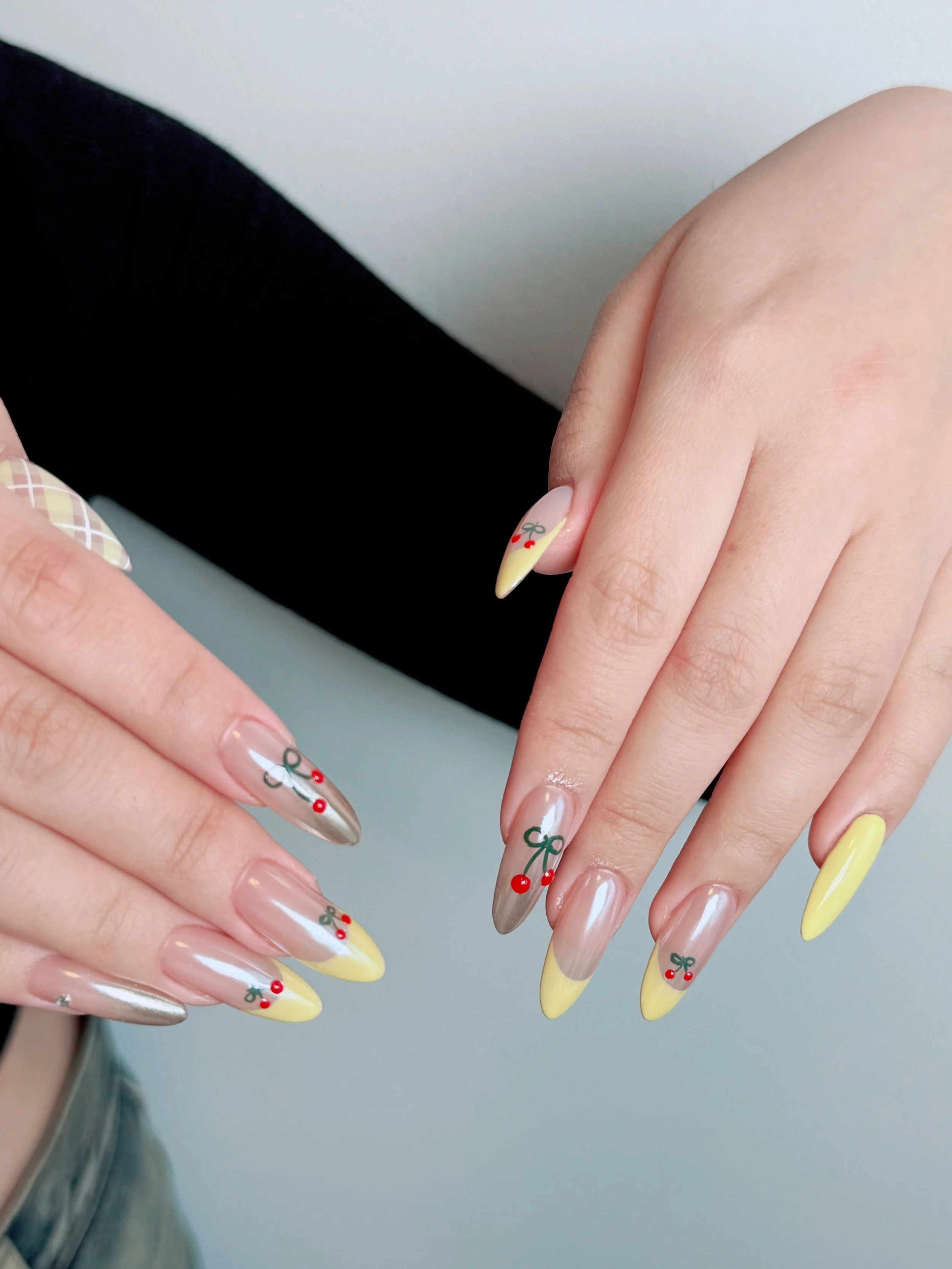 Nail art with yellow tips and holiday-themed designs, including red cherries and green bows.