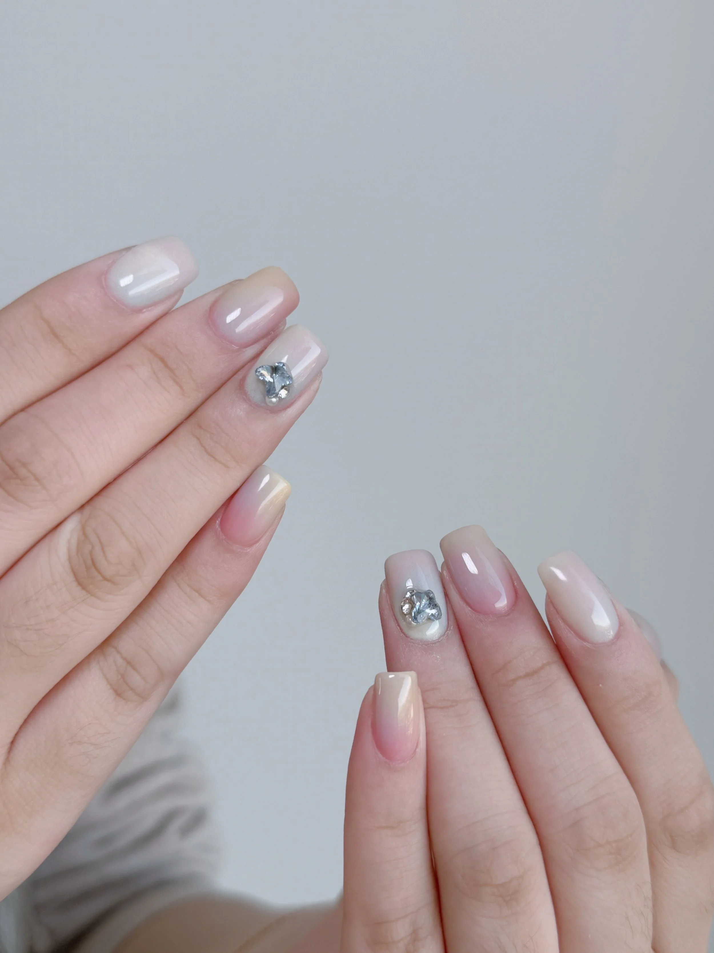 Close-up of hands with manicured nails, featuring clear gloss polish and silver rhinestone nail art on index fingers.