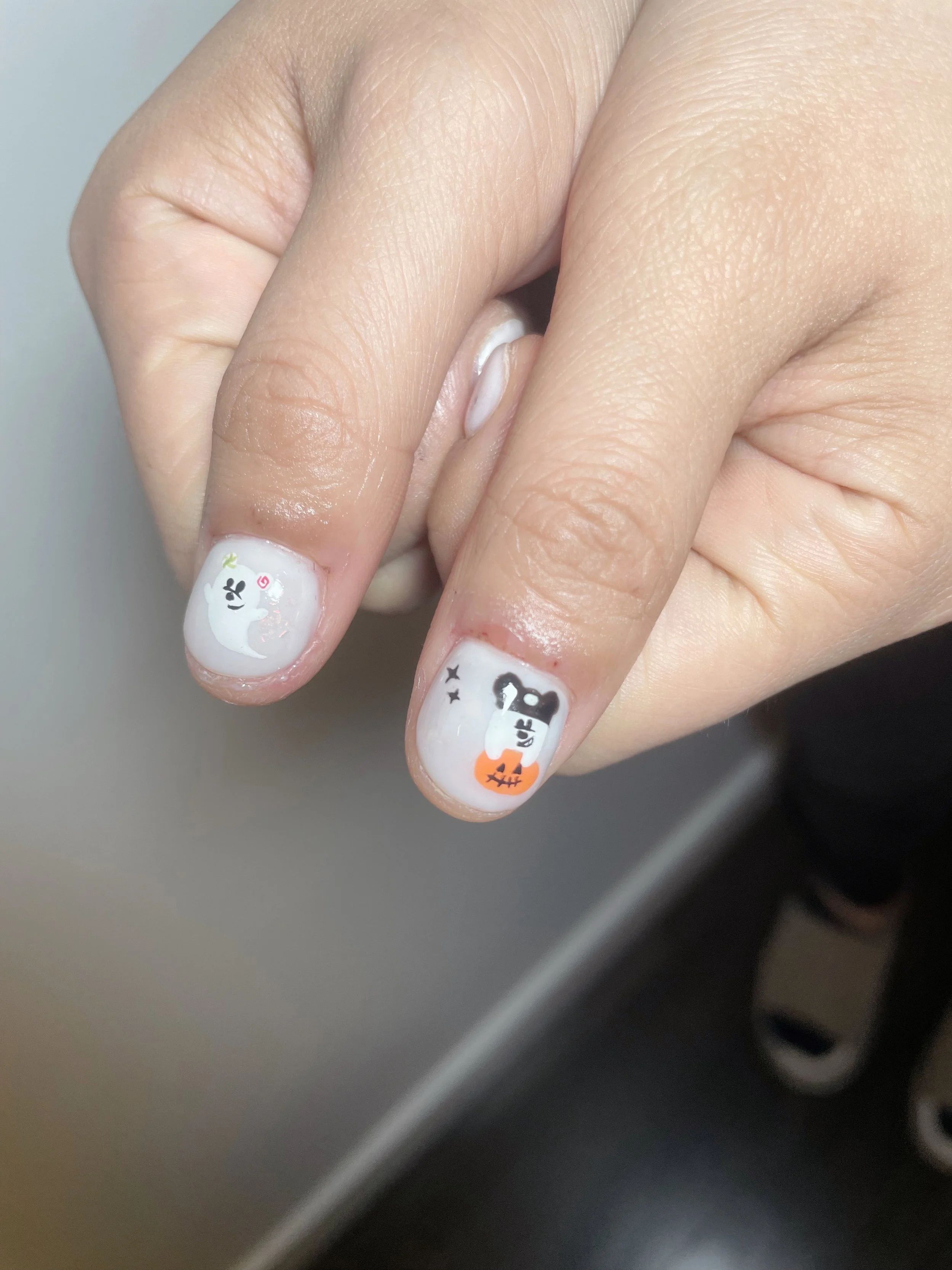 Nail art featuring Halloween-themed designs with a ghost on the thumb and a dog with a pumpkin on the index finger.